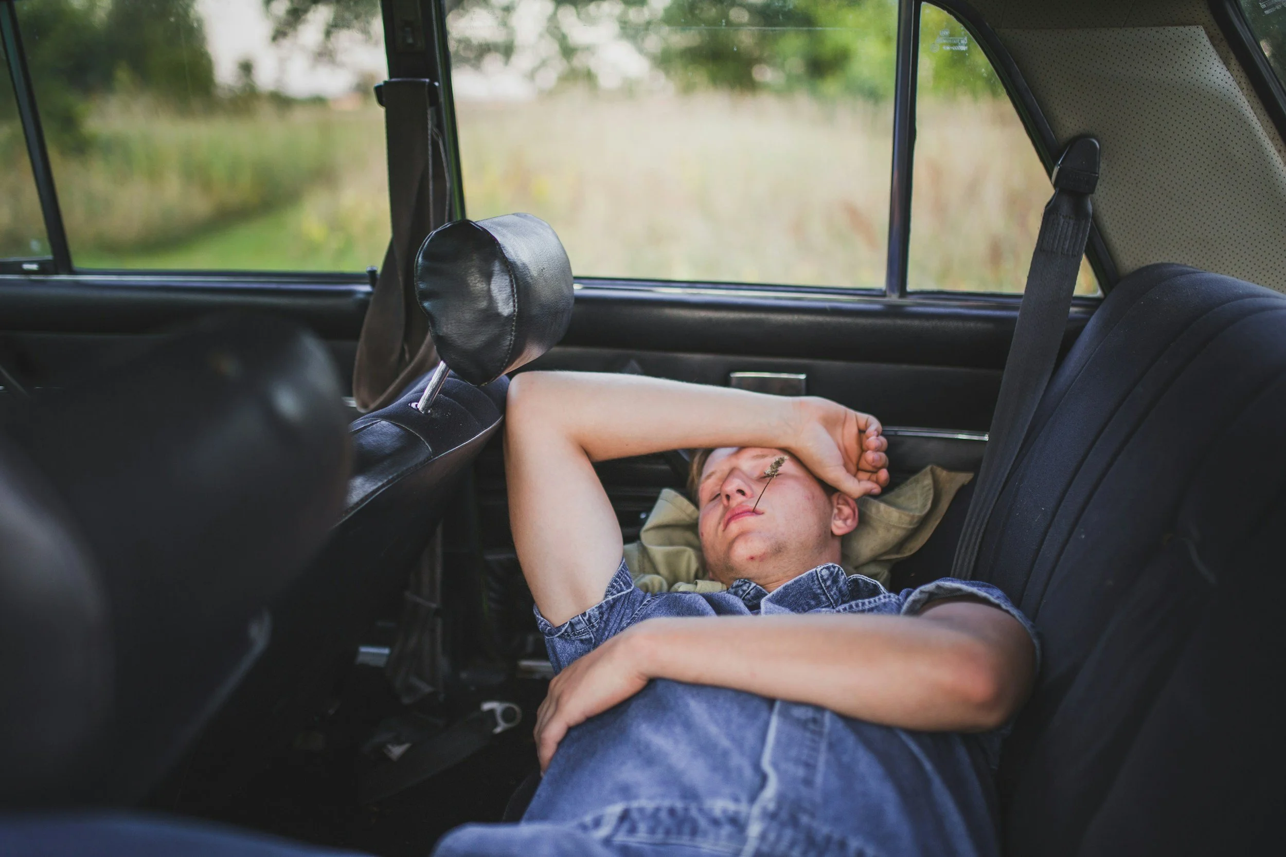 Young man sleeping the the back seat of a car with a straw hanging out of his mouth