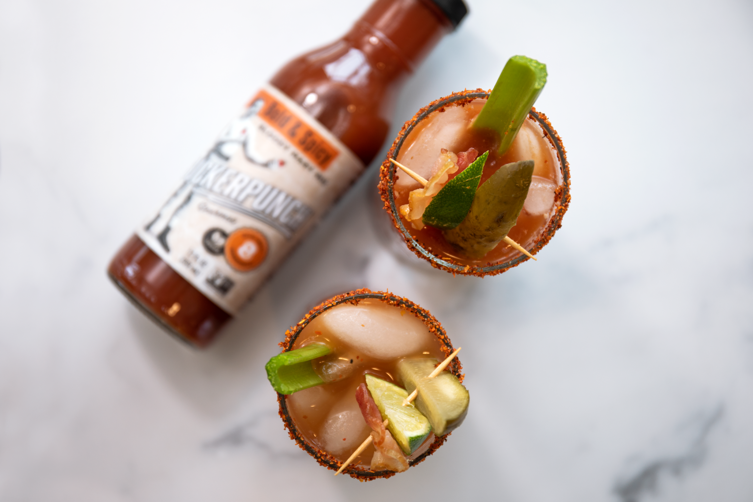 shot of two bloody marys in glasses from the top angle.  There is a Hot sauce bottle on it's side in the background