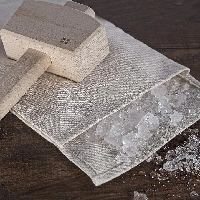 An undeyed burlap bag filled with crused ice and resting on a wooden table.  The mallet of unstained wood is laying across the top of the mallet.