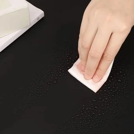 A black silicone mat with liquid spilled on it.  Someone is using a napkin to wipe a clear path through the liquid to demonstrate how easy it is to clean