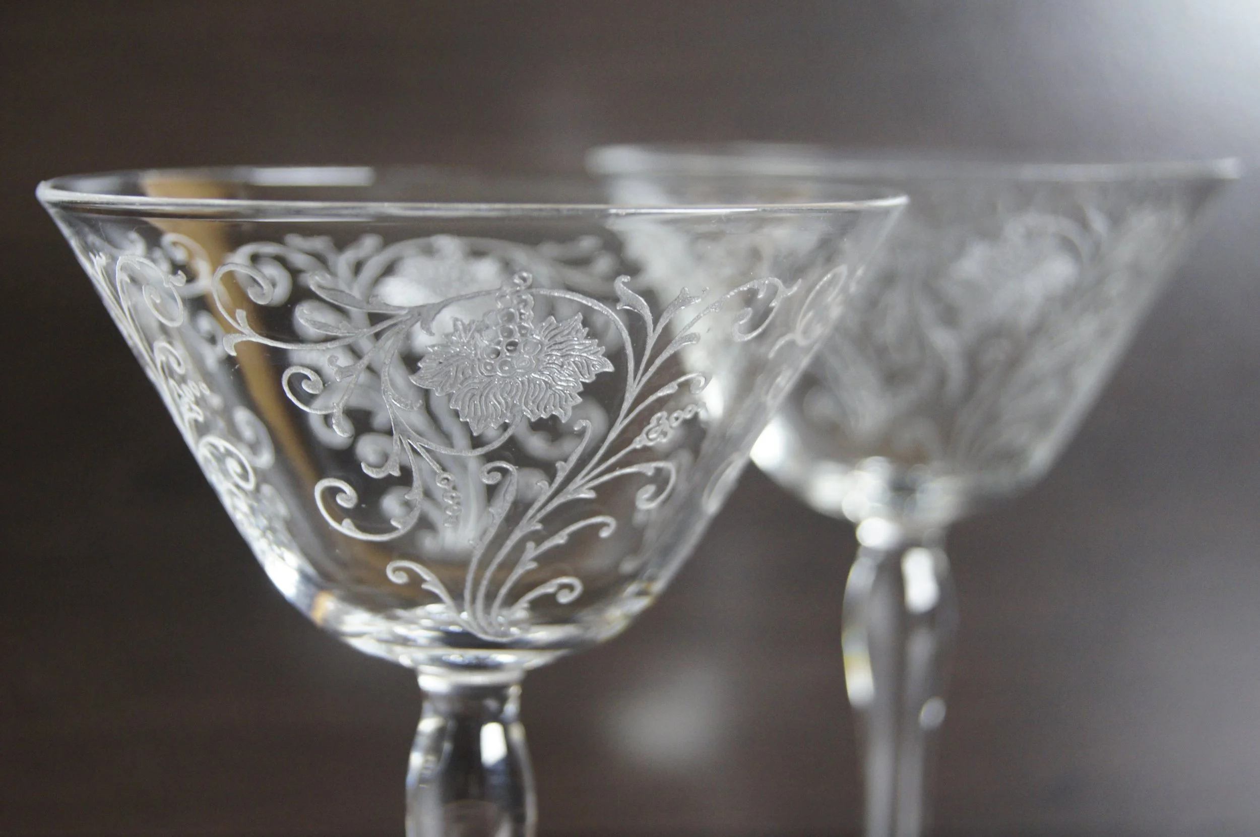 Two small martini glasses with floral etchings on them.  Both are empty.