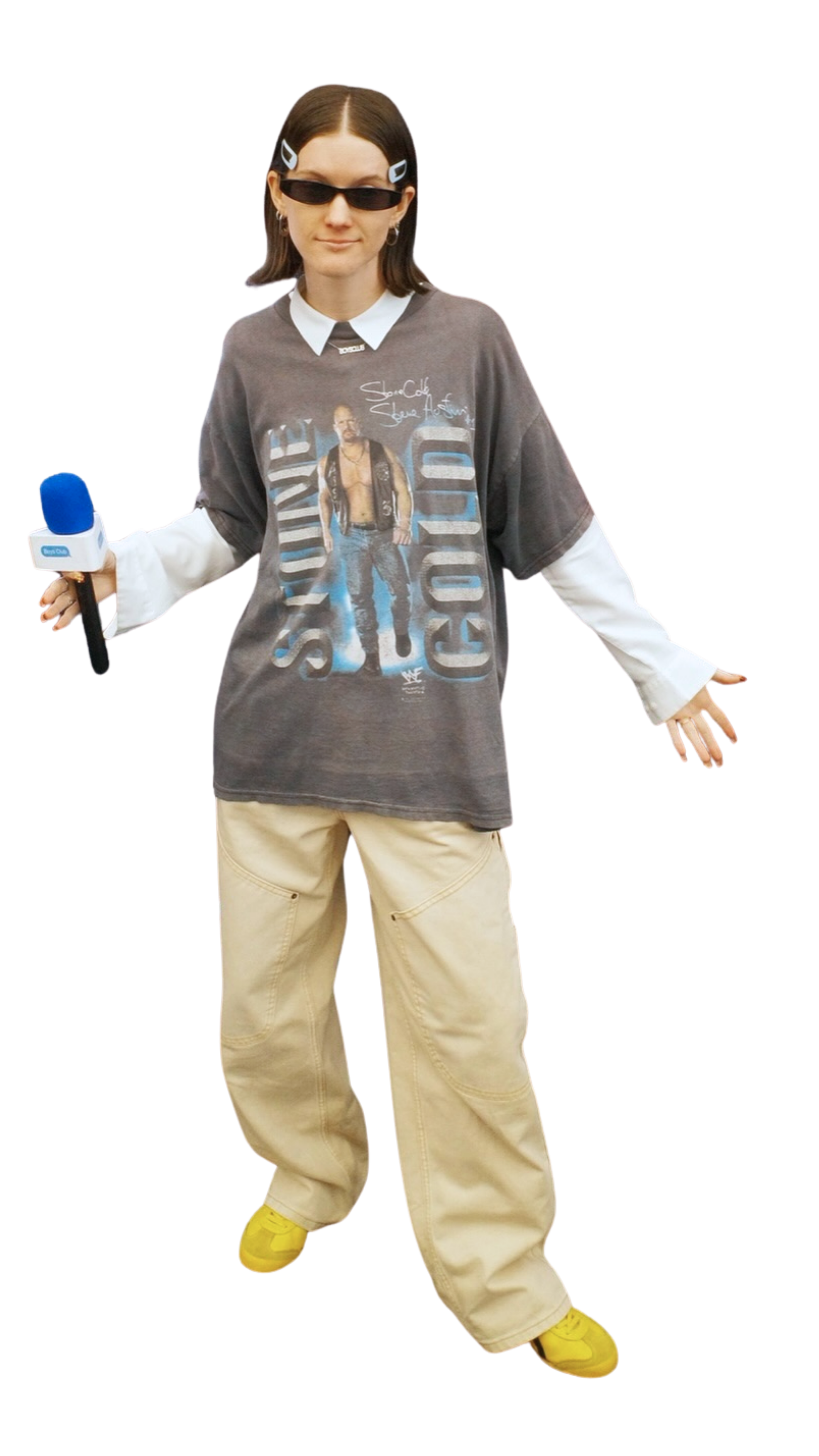 A young woman with brown hair wearing black sunglasses, a graphic T-shirt featuring a male wrestler, off-white cargo pants, yellow shoes, and holding a microphone with a blue foam cover.