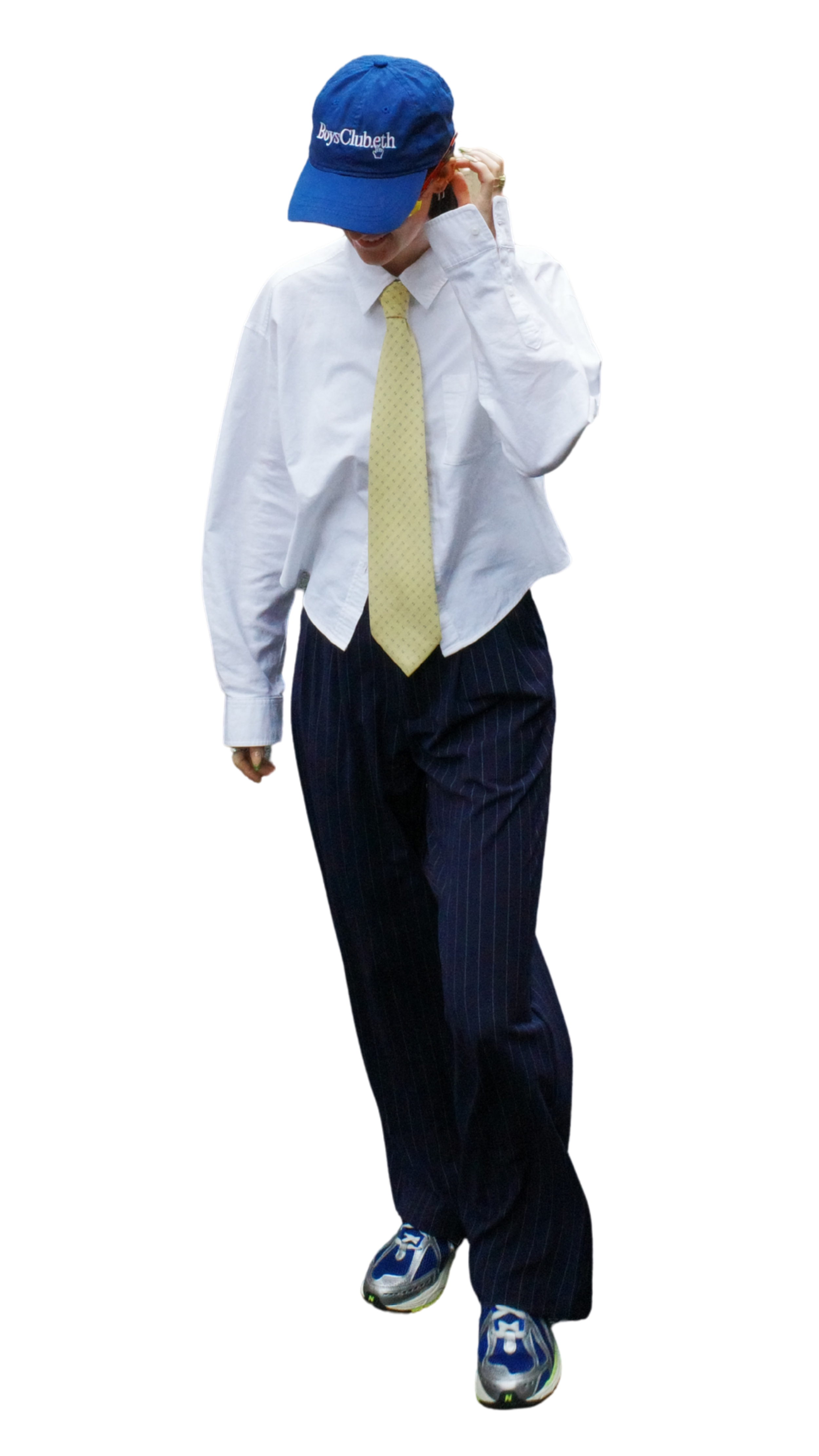 Person wearing a blue cap with 'BoysClub.eth' written on it, a white shirt, a yellow tie, striped dark pants, and sneakers, walking and adjusting their earring.