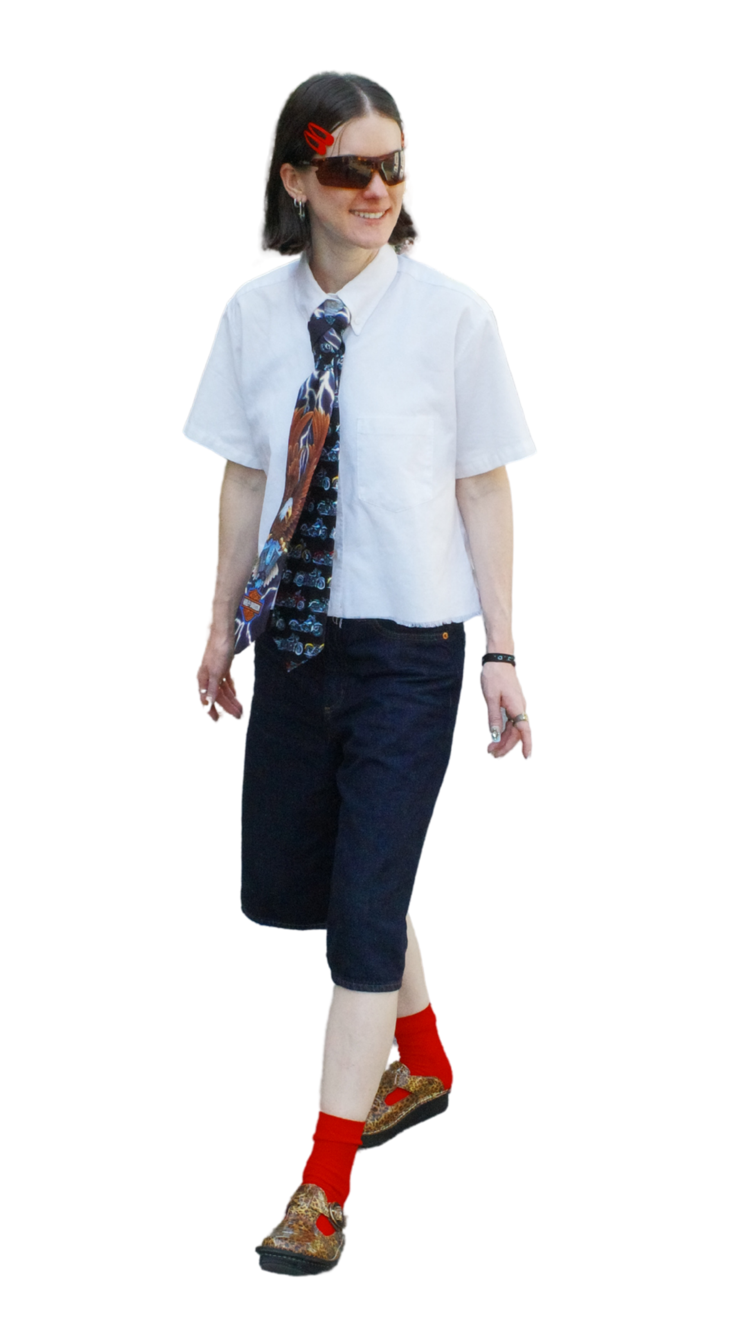 A person walking wearing sunglasses, a white tied shirt, dark pants, red socks, and leopard-print shoes, with a patterned tie and a red hair clip.