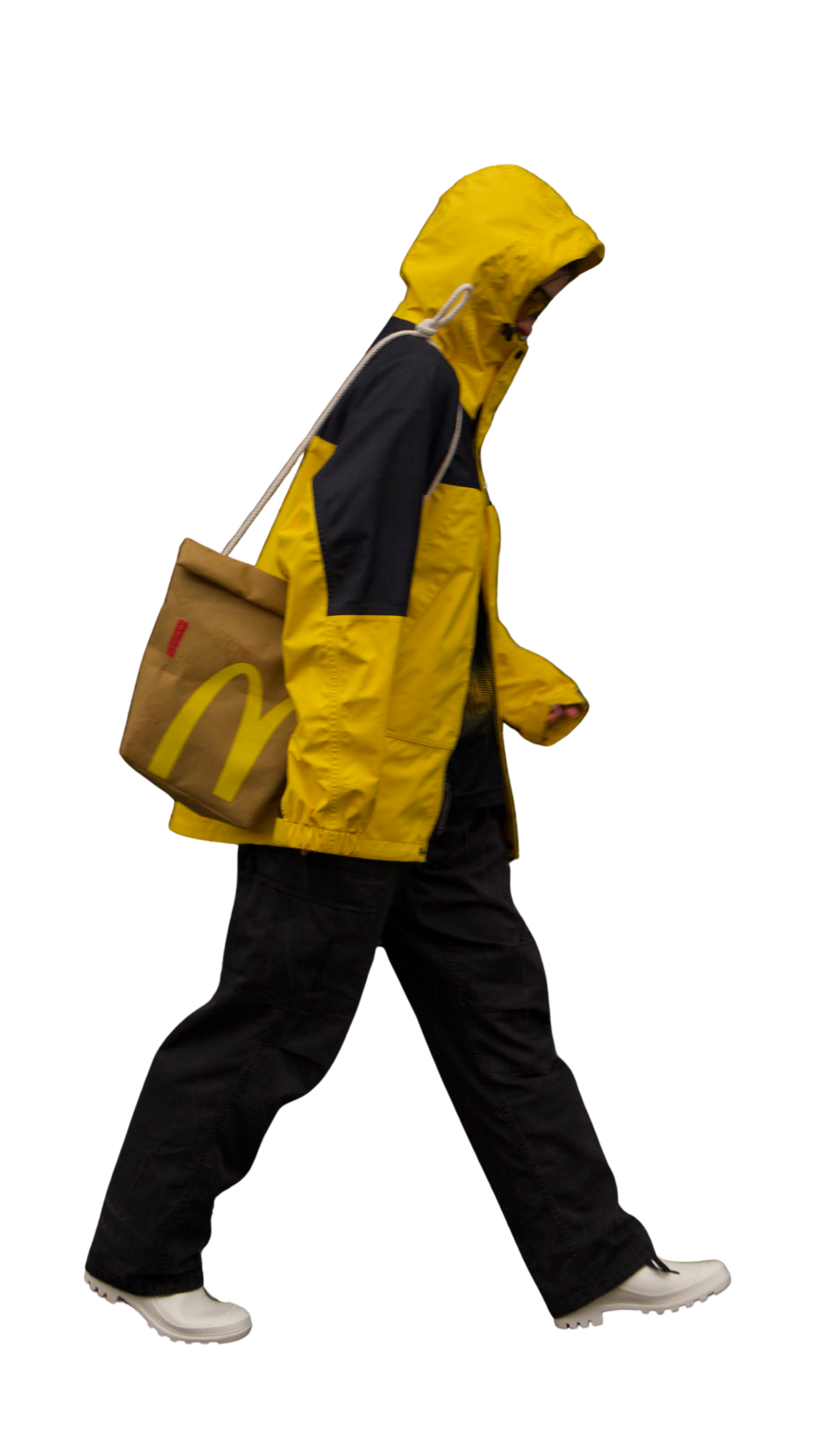 Person walking with a yellow and black rain jacket, black pants, white shoes, and a McDonald's takeaway bag, against a black background.
