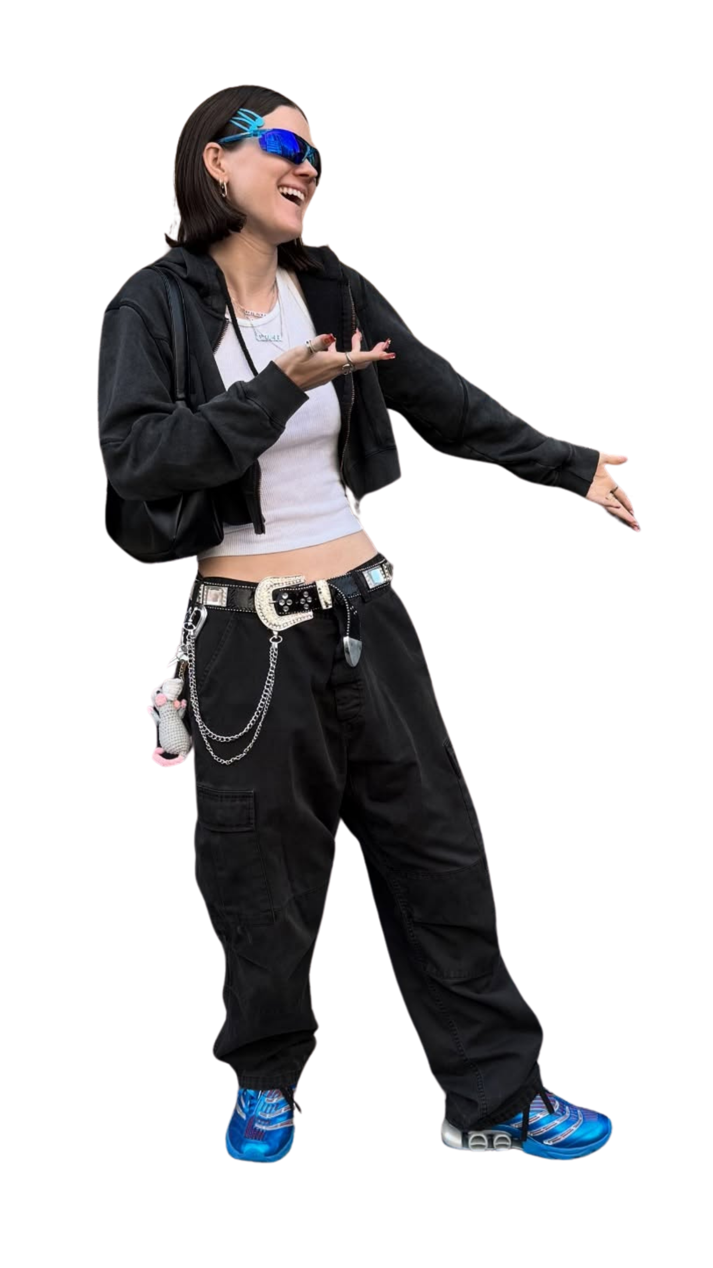 Young woman wearing black cargo pants, a leather belt, a cropped white shirt, a black hoodie, and blue athletic shoes, confidently gesturing with her right hand, laughing, and wearing reflective blue sunglasses with a futuristic design.