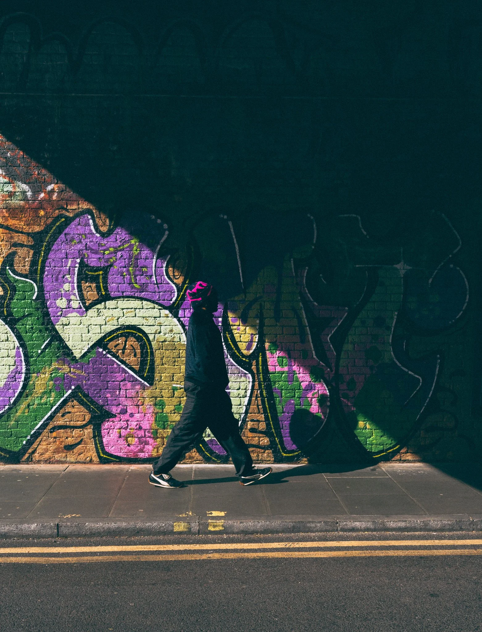 A person walking past a colorful graffiti mural on a brick wall at night.