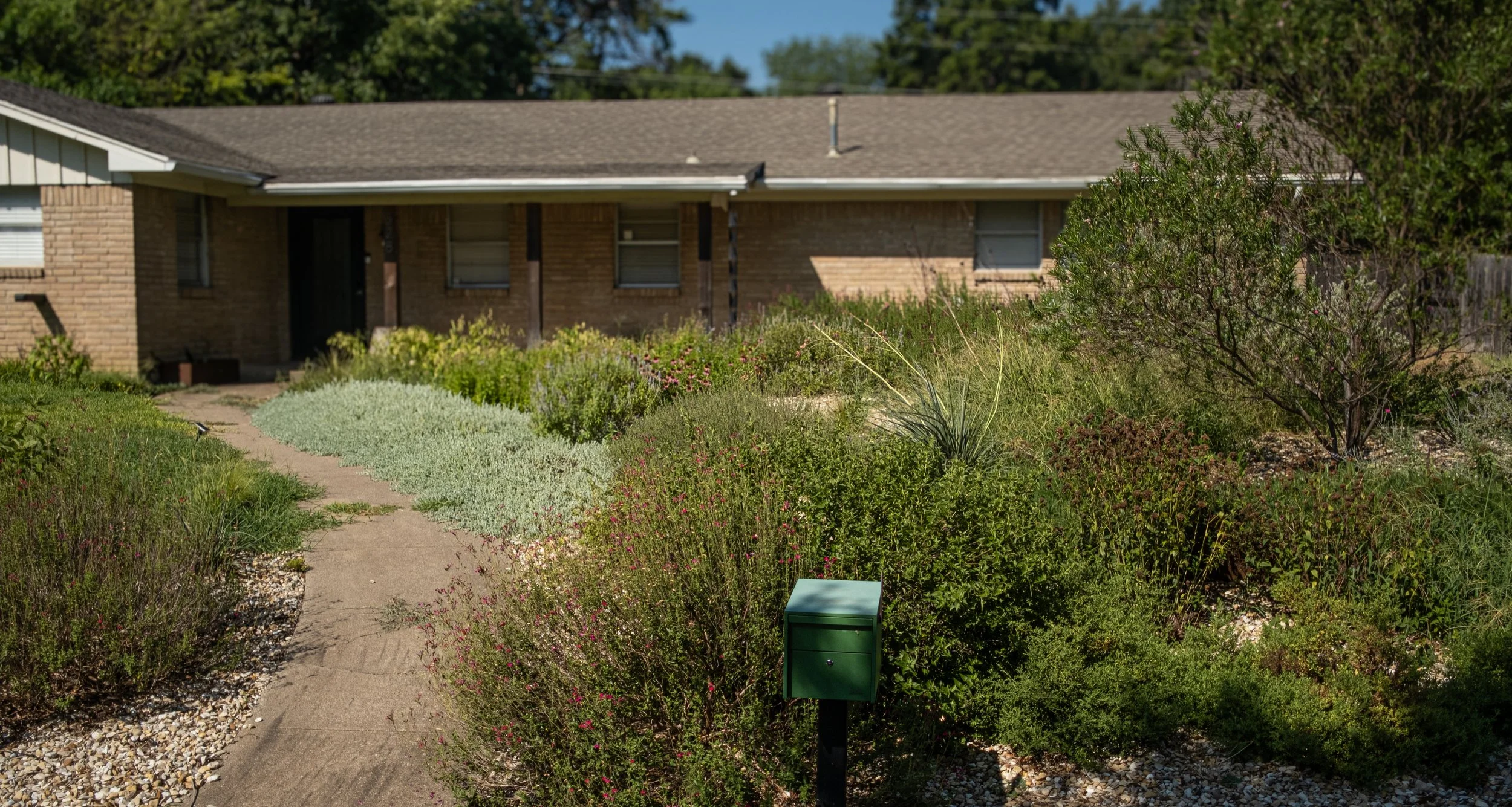 Front yard of a brick house with a garden, pathway, and bushes.