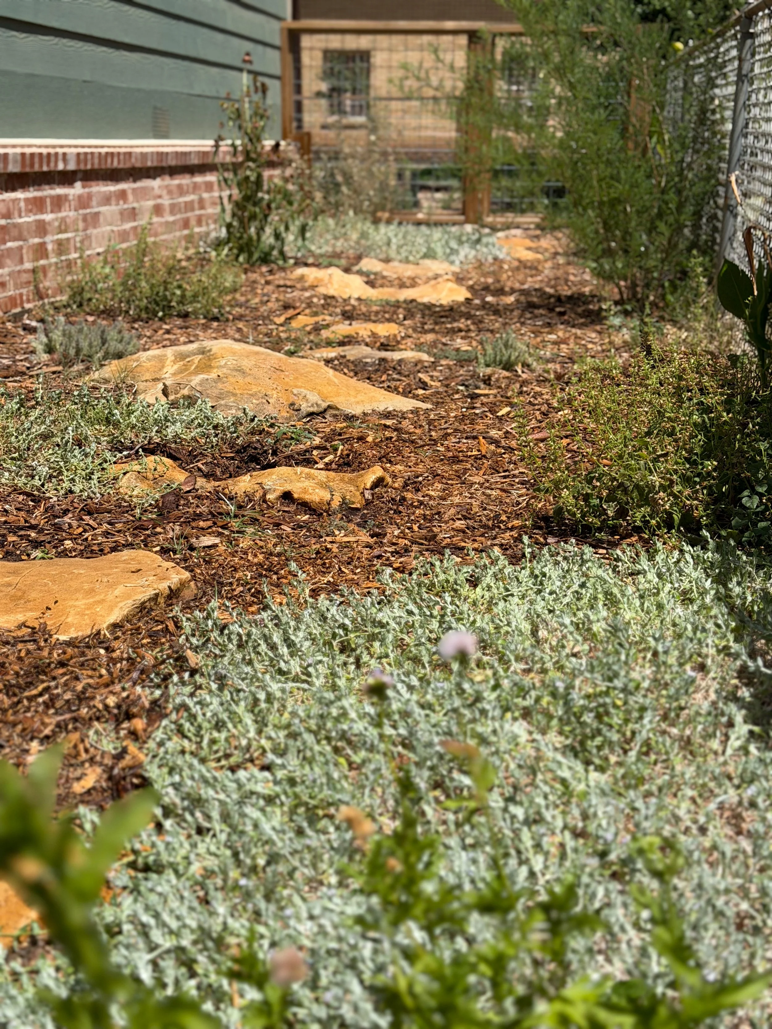 A backyard garden with rocks, plants, a brick wall, and a wooden fence.