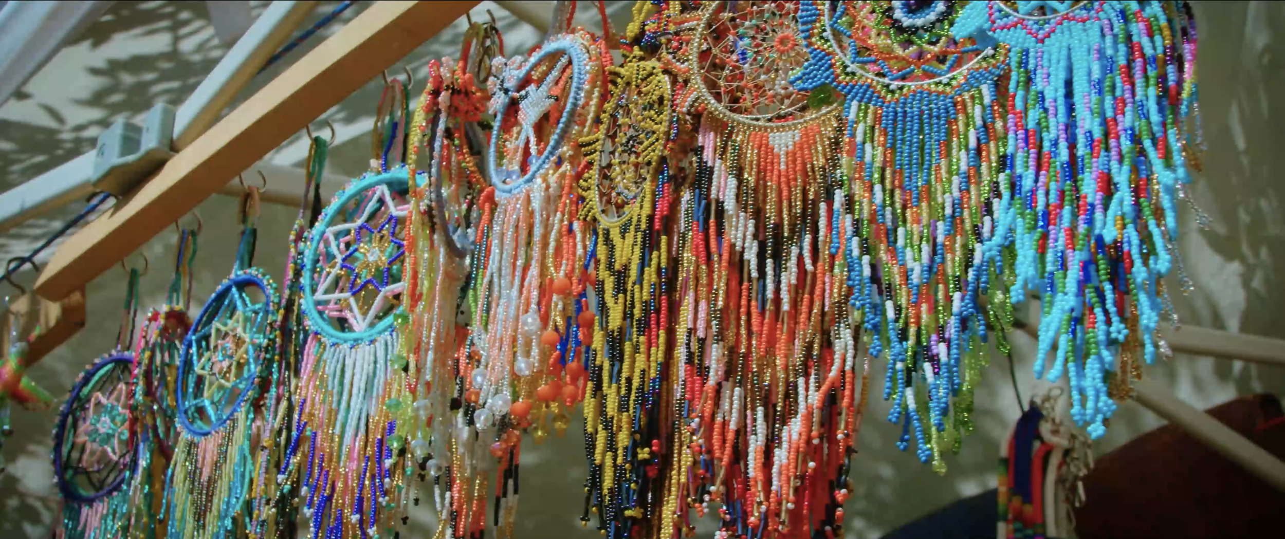 Colorful beaded jewelry, including Native American handicraft, necklaces, and dreamcatchers, hanging on a wooden display rack.