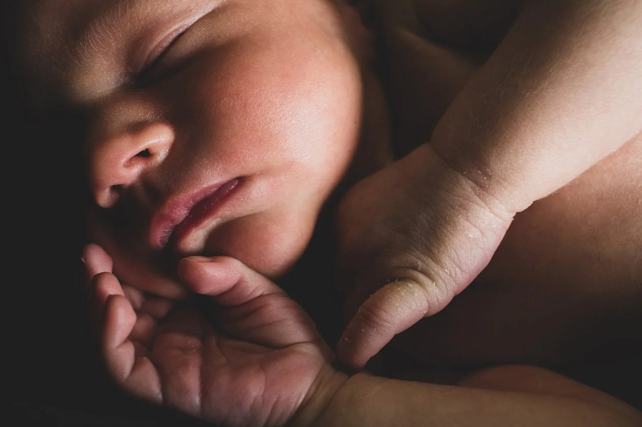 Close-up of a newborn baby peacefully sleeping, with a hand gently touching their face.