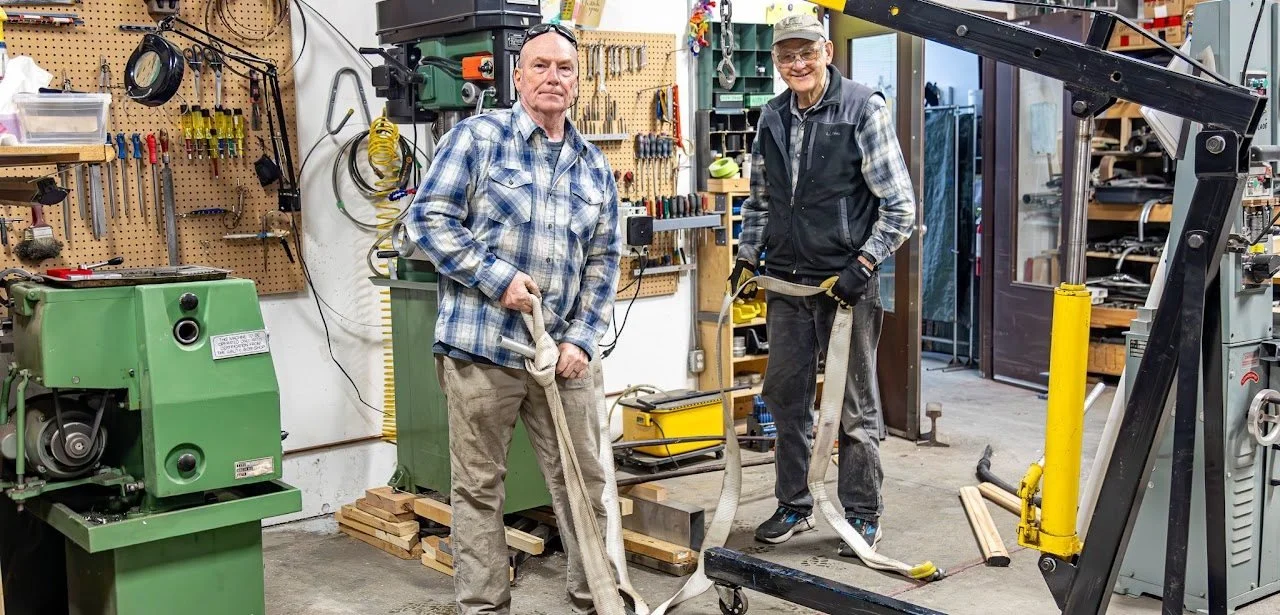 Two volunteers using a shop crane and hoist strap in the Ability Workshop