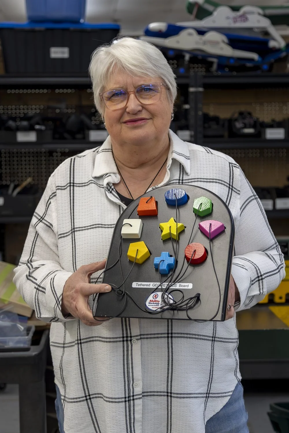 Nancy Wiebe, Ability Workshop board member, holding a custom sensory switch board with colourful buttons
