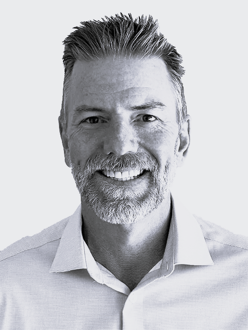 A smiling middle-aged man with short styled hair, a beard, and a mustache, wearing a collared shirt.