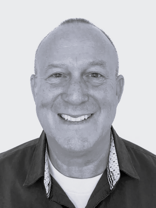 Black and white headshot of smiling man with short hair, wearing a collared shirt and jacket against a plain background.