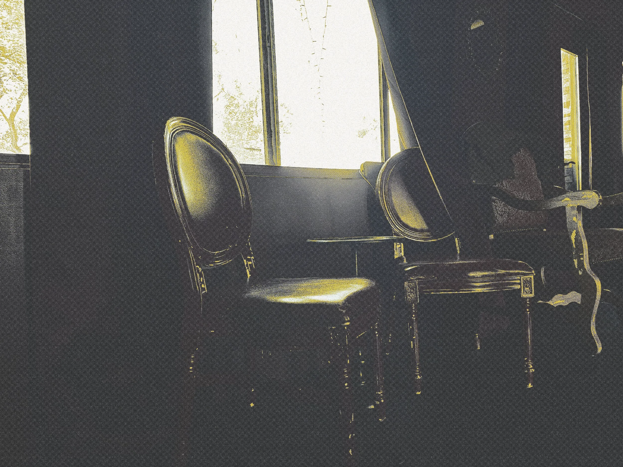 A dark room with a large window showing trees outside. Four chairs are positioned in front of the window, and there are reflections of string lights on the floor.
