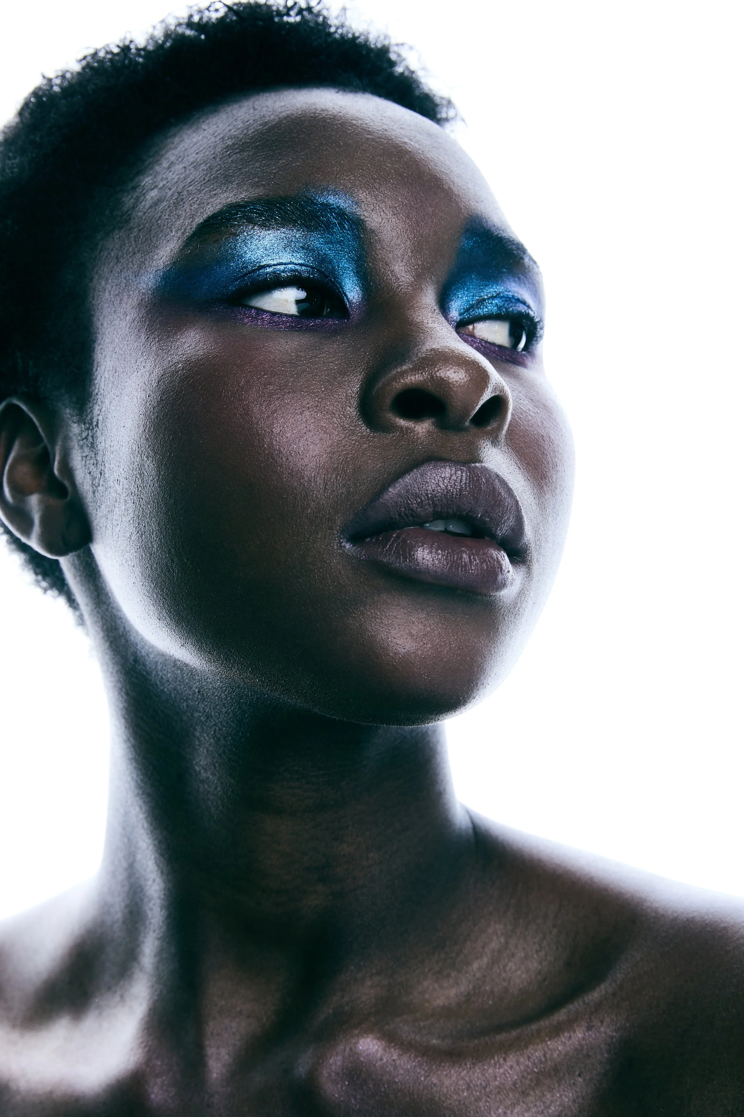 Primer plano de rostro de mujer con maquillaje en ojos y piel oscura, fondo blanco.