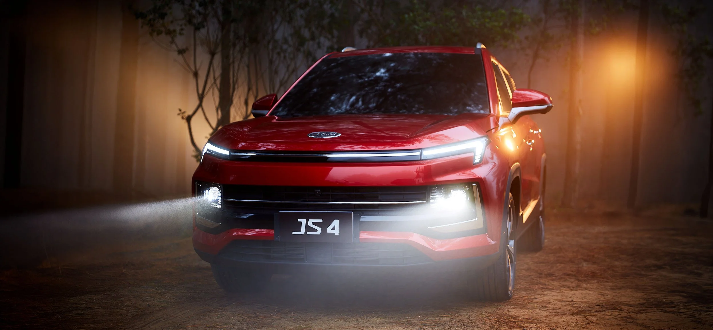 Auto rojo con luces encendidas en un camino rodeado de árboles durante la noche.