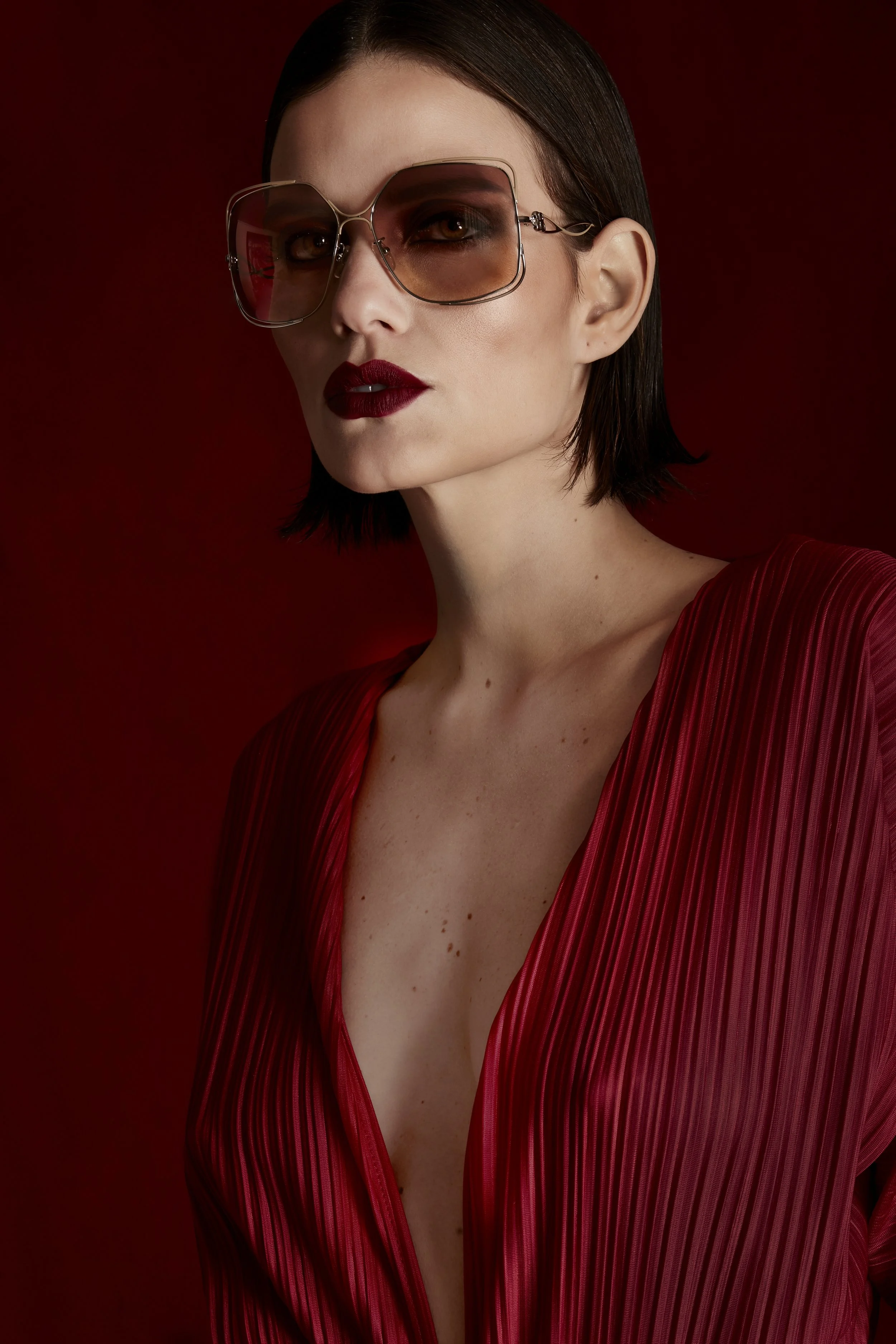Mujer con gafas de sol grandes, maquillaje oscuro y labios rojos, vestida con un vestido rojo con rayas.