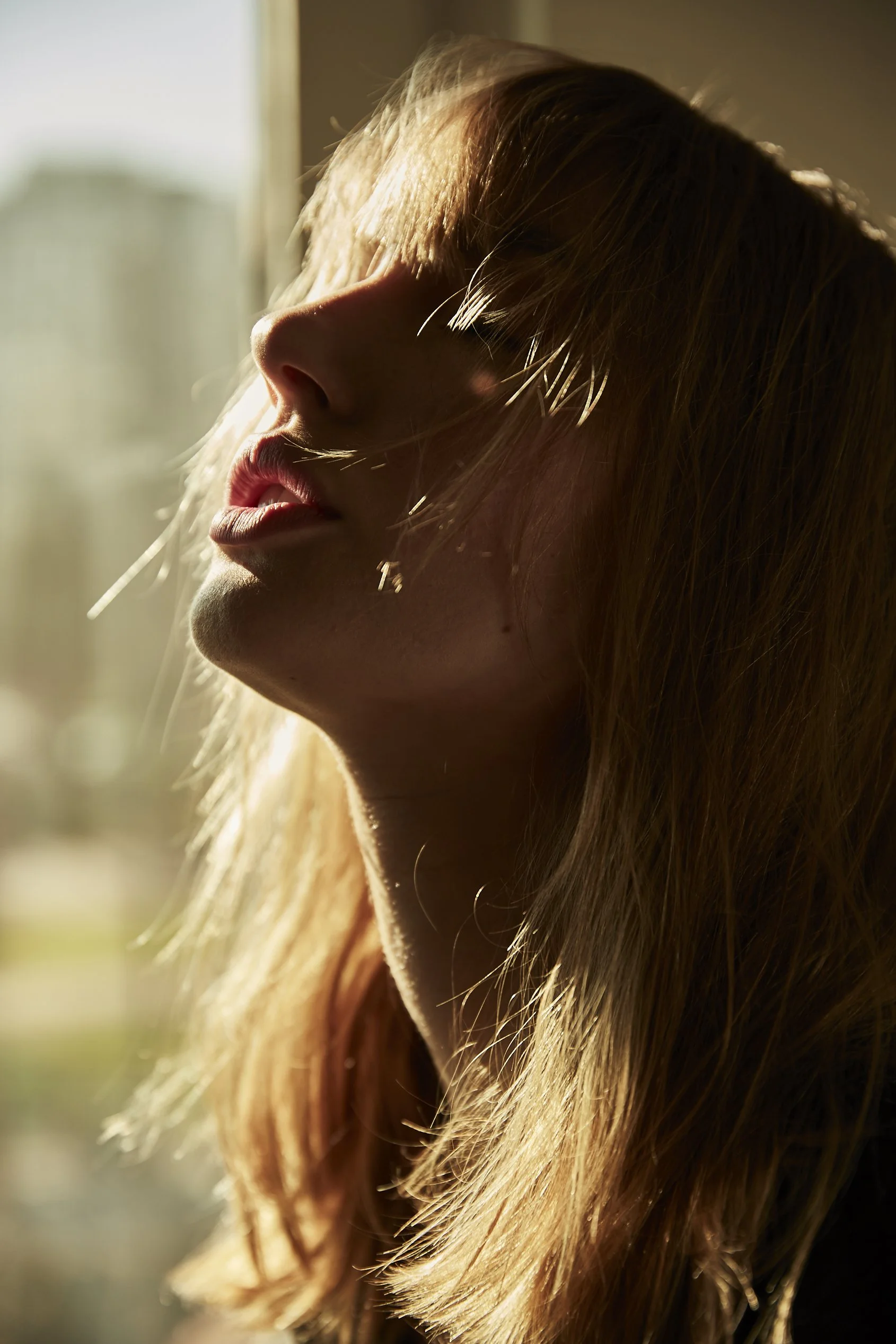 Primer plano de la cara de una mujer con cabello largo y rubio, parcialmente cubierto por el cabello, con luz suave y cálida.