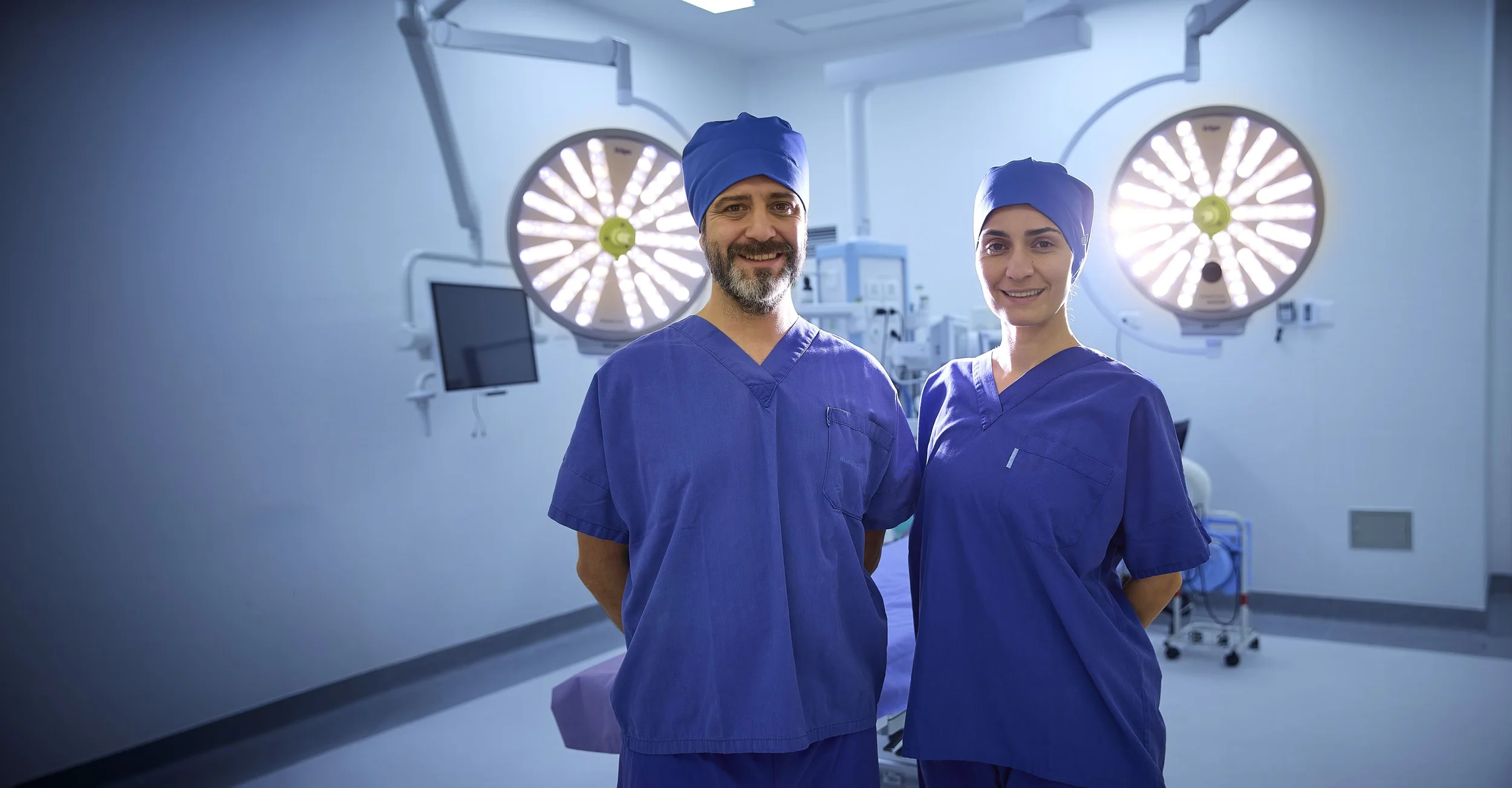Dos cirujanos en un quirófano con luz quirúrgica y equipo médico.