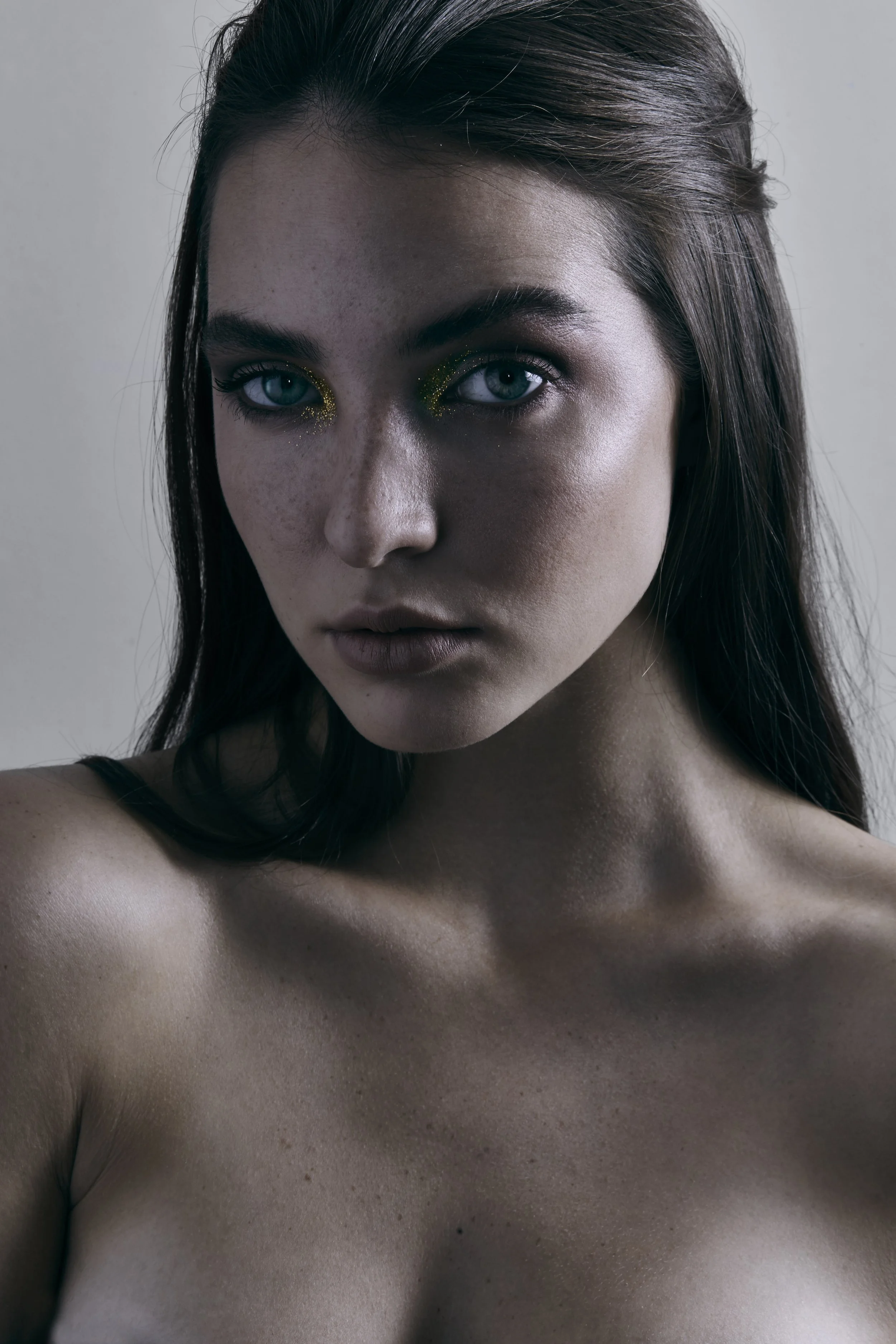 Primer plano de rostro de mujer con cabello oscuro, ojos llamativos con delineado dorado brillante y piel con pecas, sin ropa visible en la imagen.