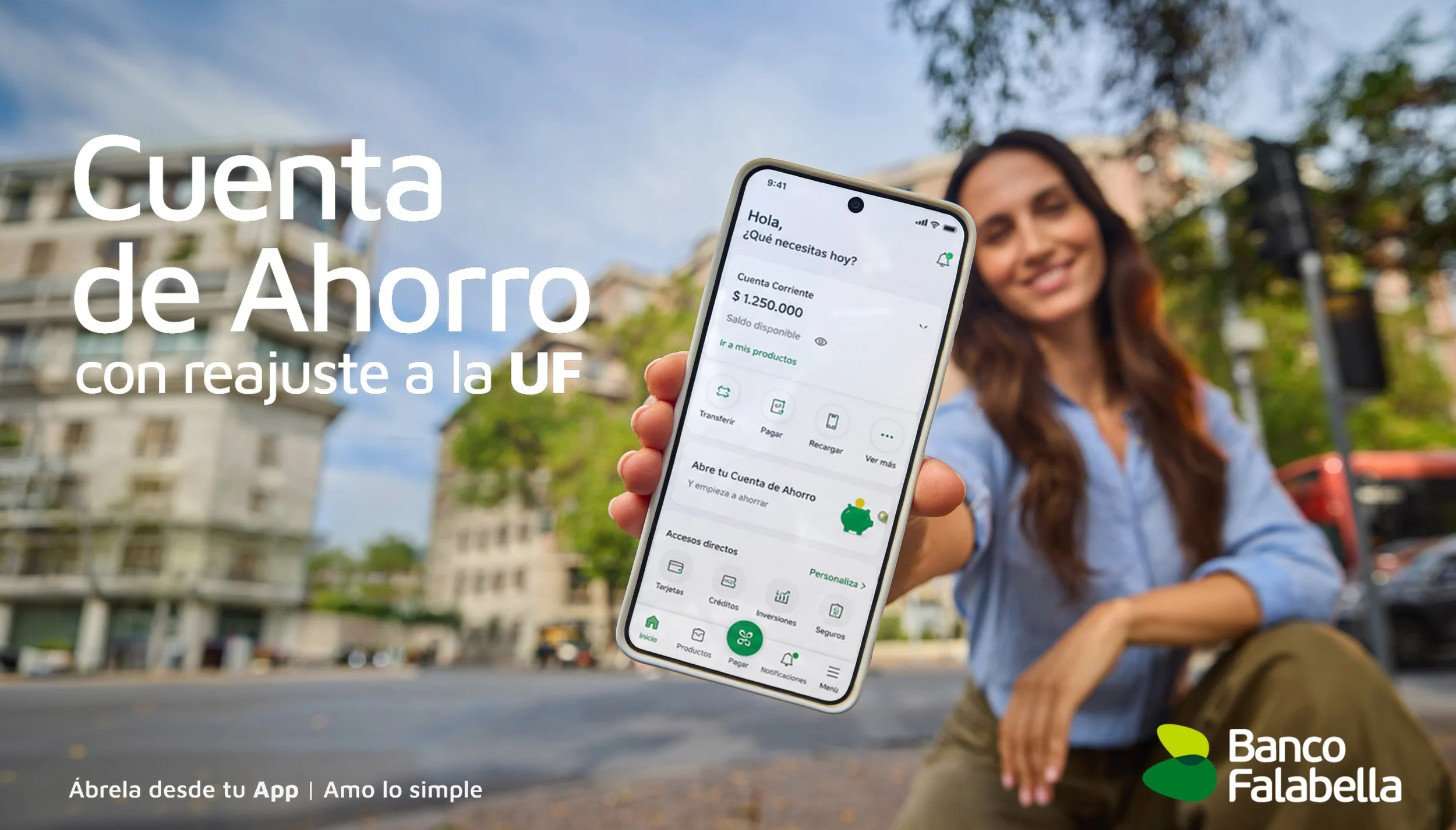 Mujer con ropa azul, sonriendo y sosteniendo un teléfono móvil mostrando la app de Banco Falabella en un entorno urbano con edificios y árboles.