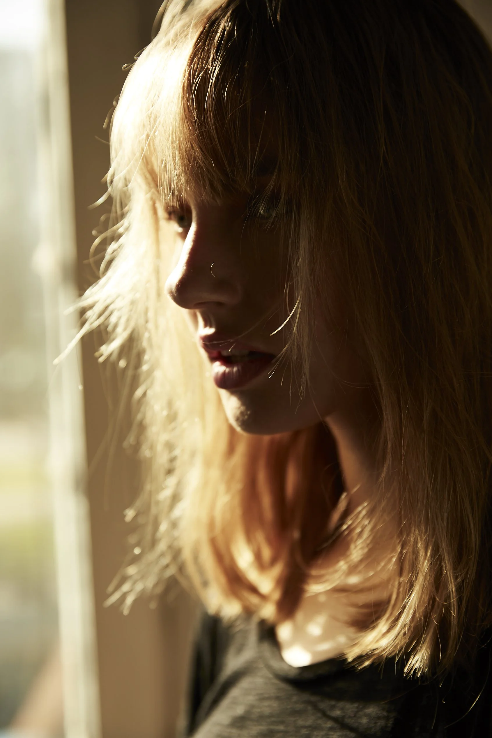 Primer plano de una mujer con cabello rubio, mirando hacia abajo y a la izquierda, con luz cálida que ilumina su rostro y cabello.