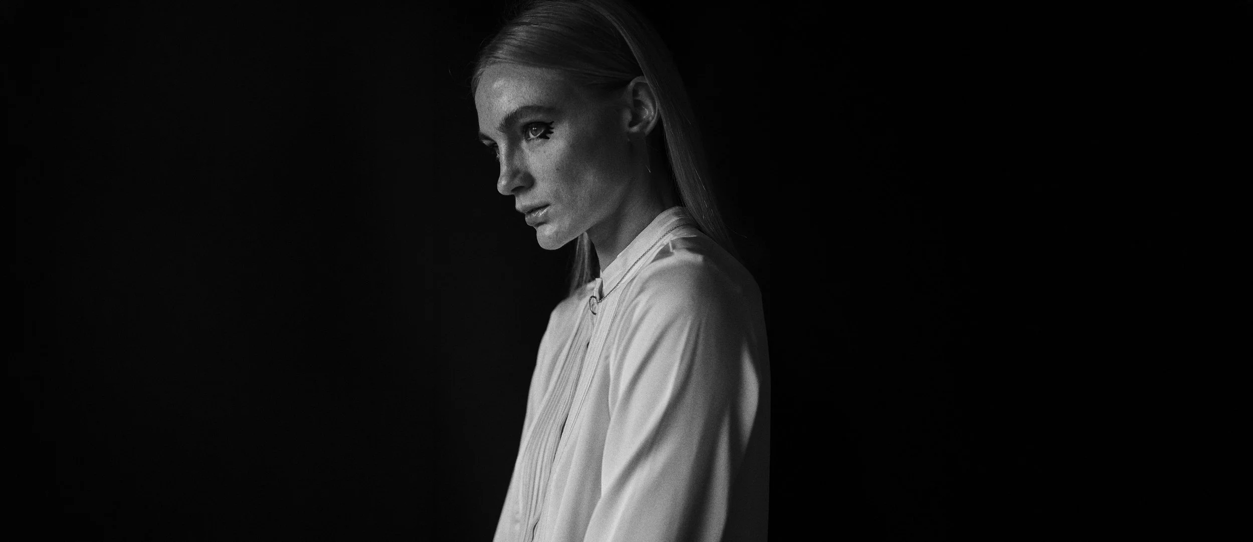 Retrato en blanco y negro de una mujer con expresión pensativa y vista de perfil, con fondo negro.