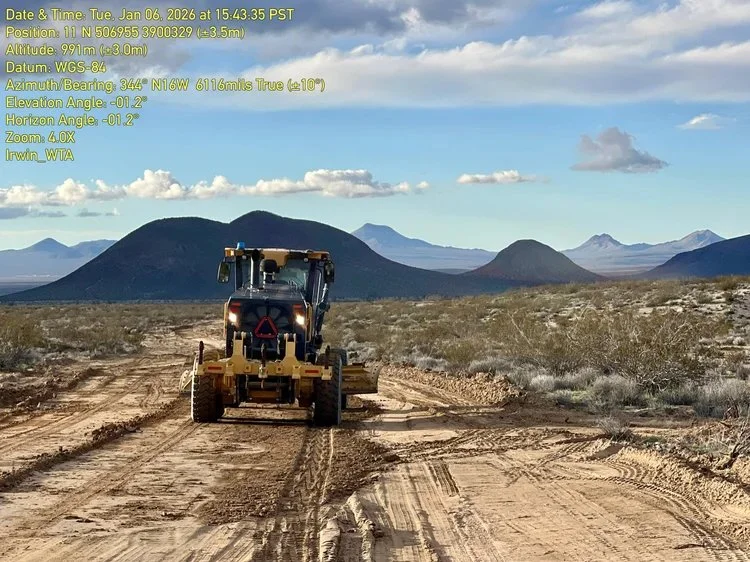 A construction vehicle on a dirt road in a desert landscape with mountains in the background under a partly cloudy sky.