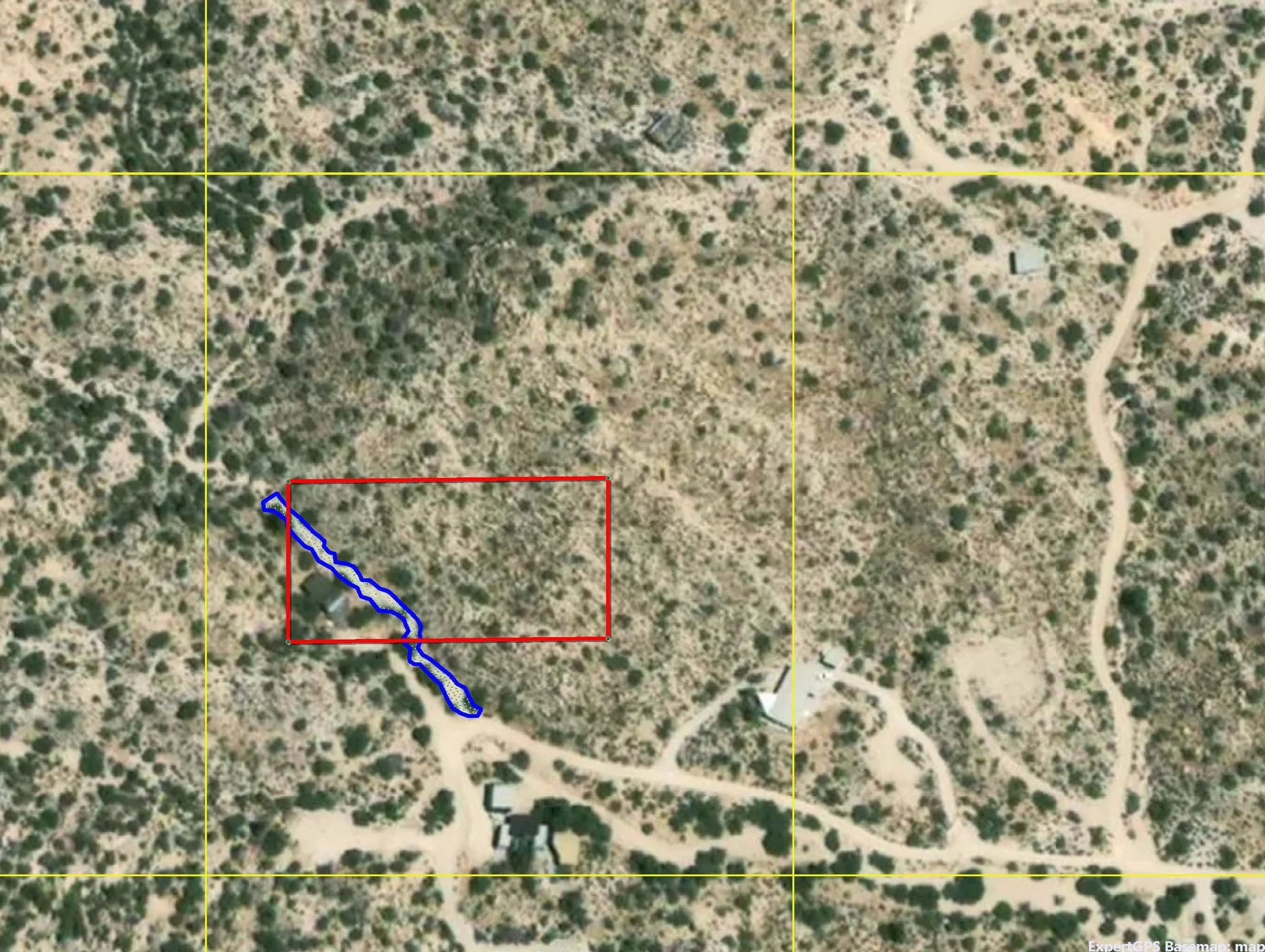 An aerial view of a rural area with a grid overlay, showing a patch of land outlined in red bounding a small winding creek and some structures nearby.