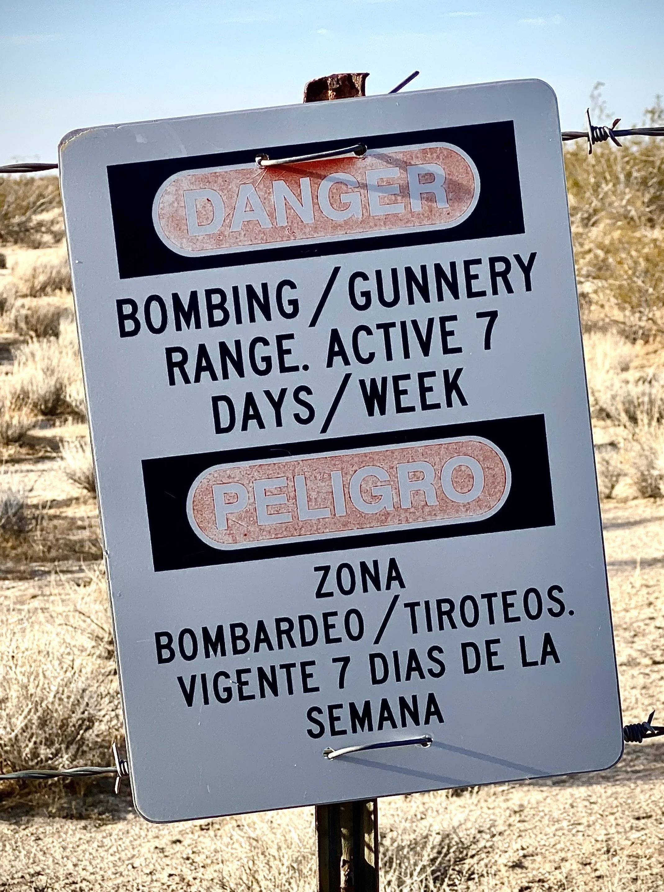 Warning sign in Spanish indicating danger from bombing or gunnery range, active for 7 days a week.