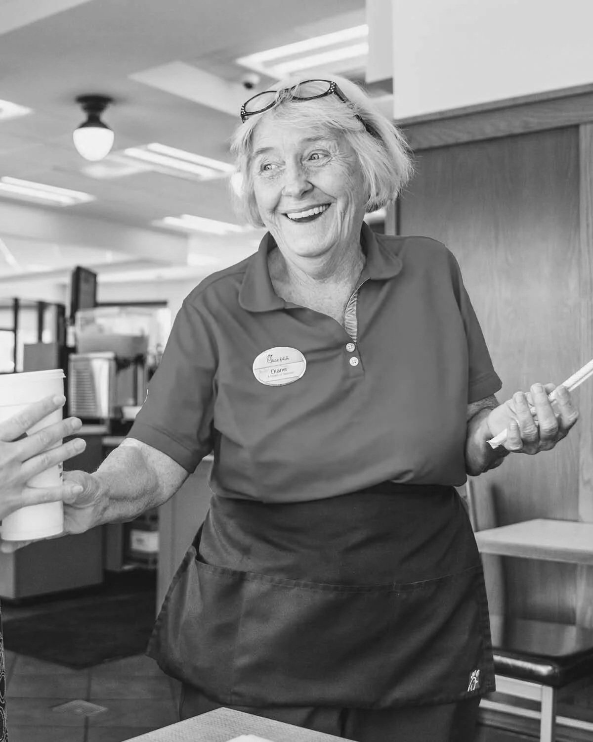 Smiling elderly woman in a uniform serving food in a cafeteria.