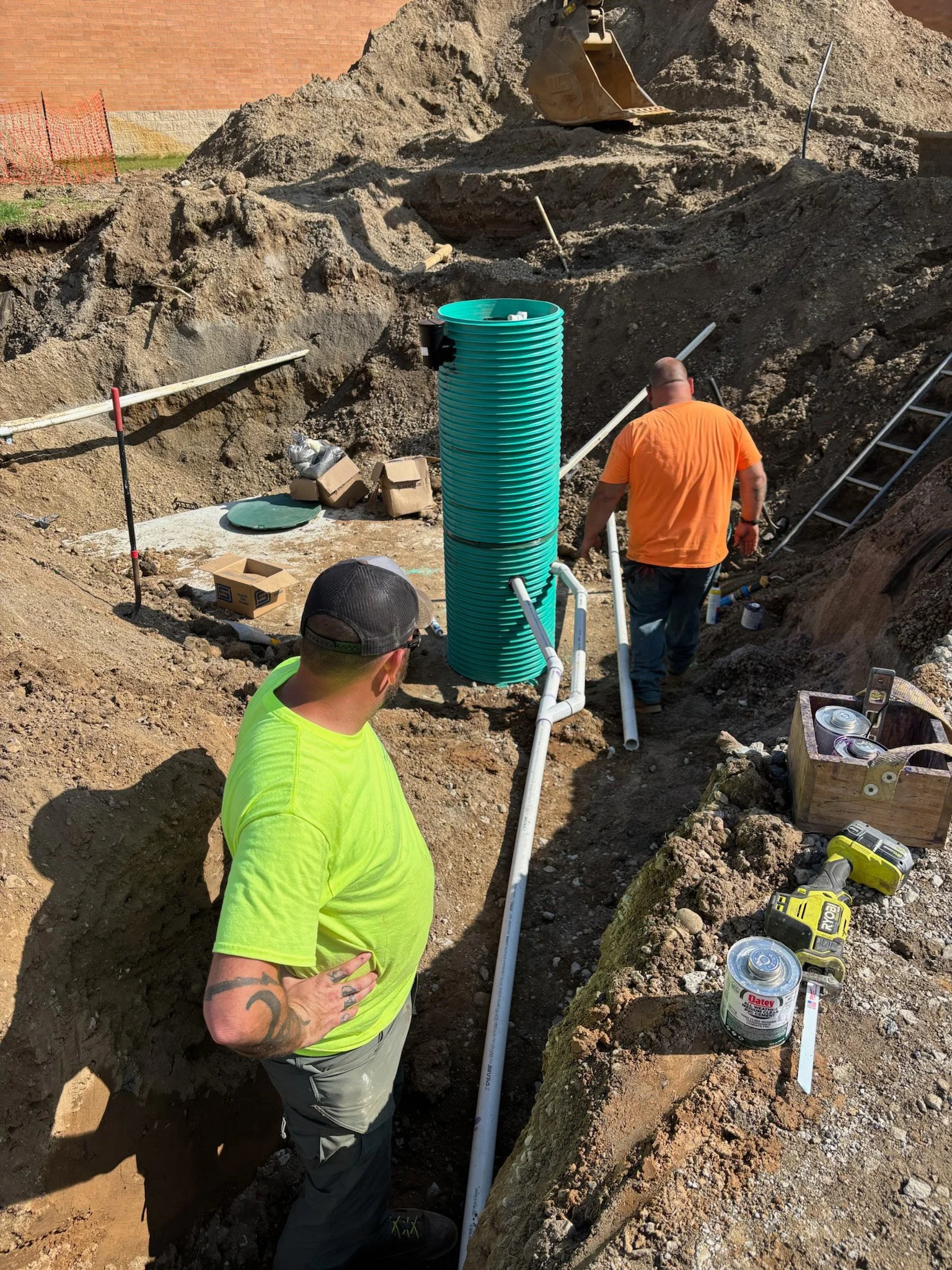 Construction workers installing underground piping in a trench at a construction site.