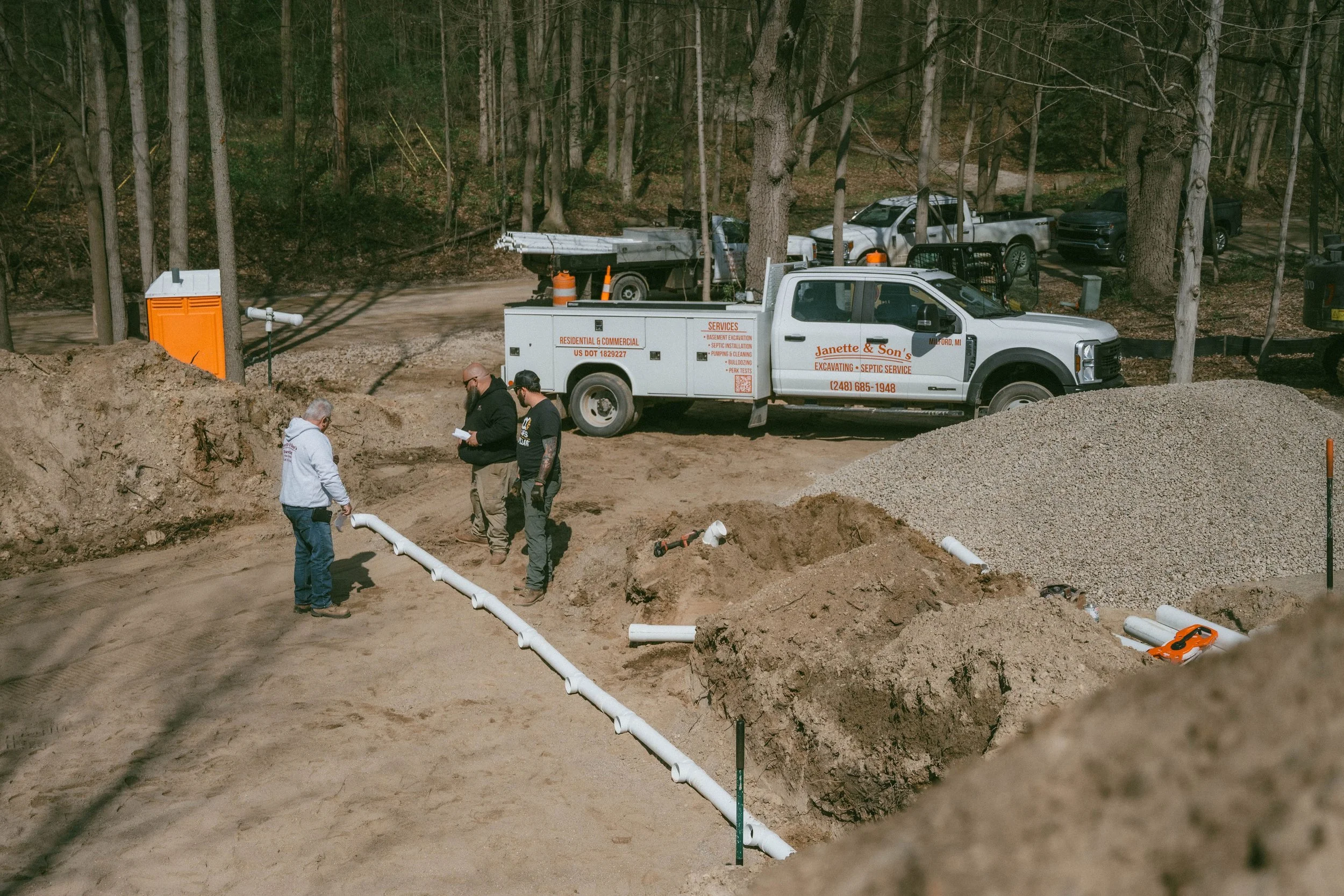 Three men working at a construction site with pipes and vehicles in a wooded area.