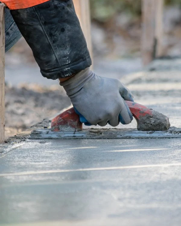 A worker's hand in a glove smoothing wet concrete with a trowel during construction.