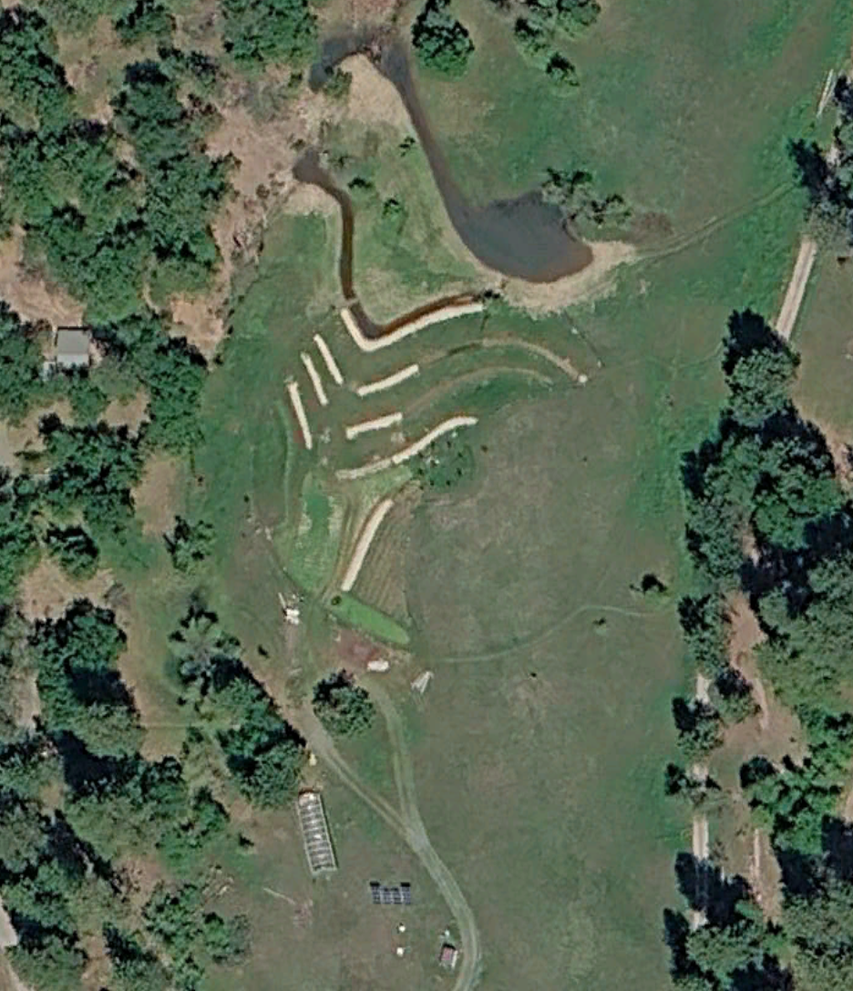 Aerial view of a landscaped outdoor area with winding pathways, a pond, and surrounding trees.