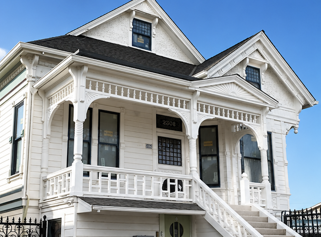 A large Victorian-style white house with detailed trim and a front porch with stairs, set against a blue sky.