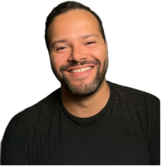 A smiling man with a beard and short hair wearing a black shirt, against a plain background.