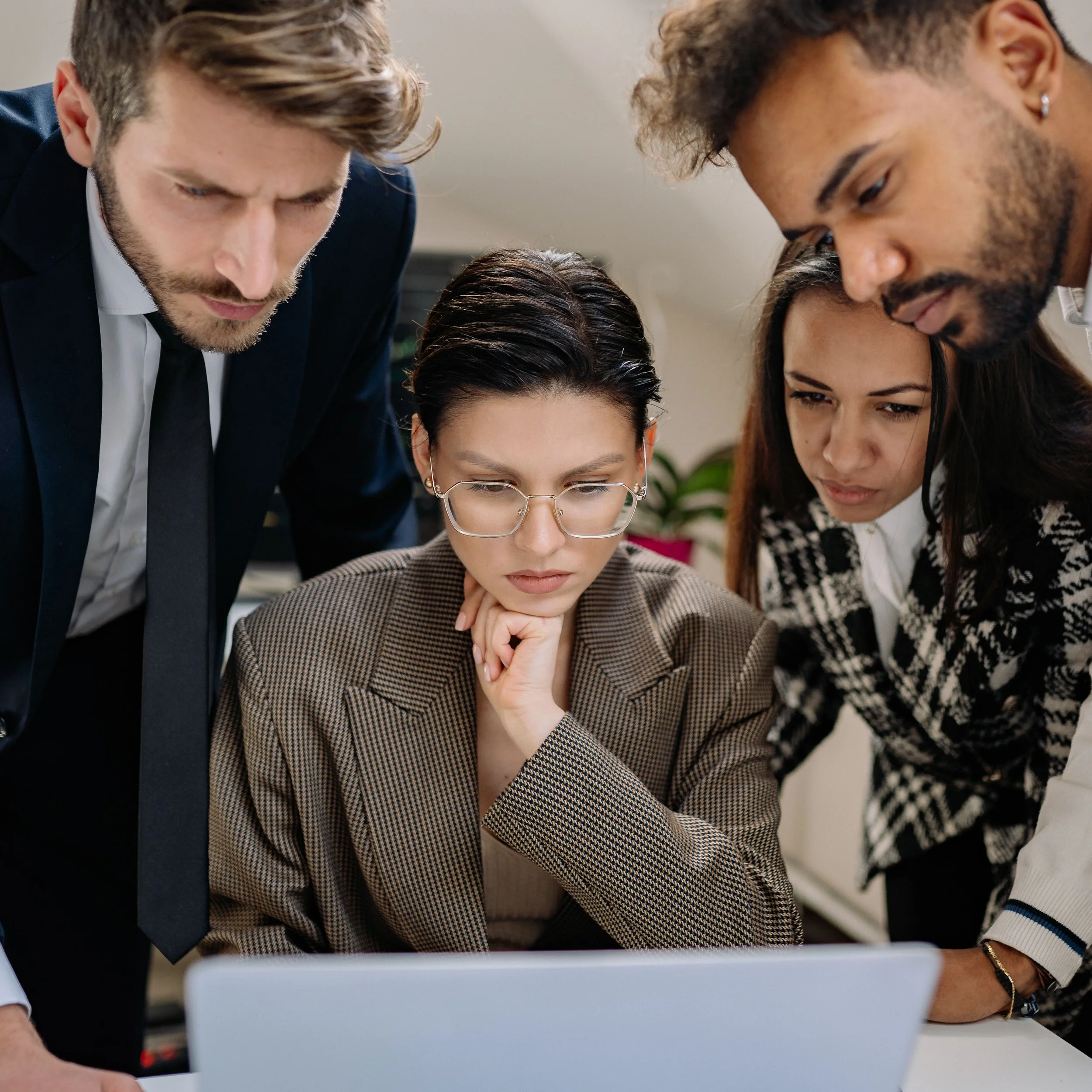 Group of diverse professionals collaborating around a laptop in an office setting.
