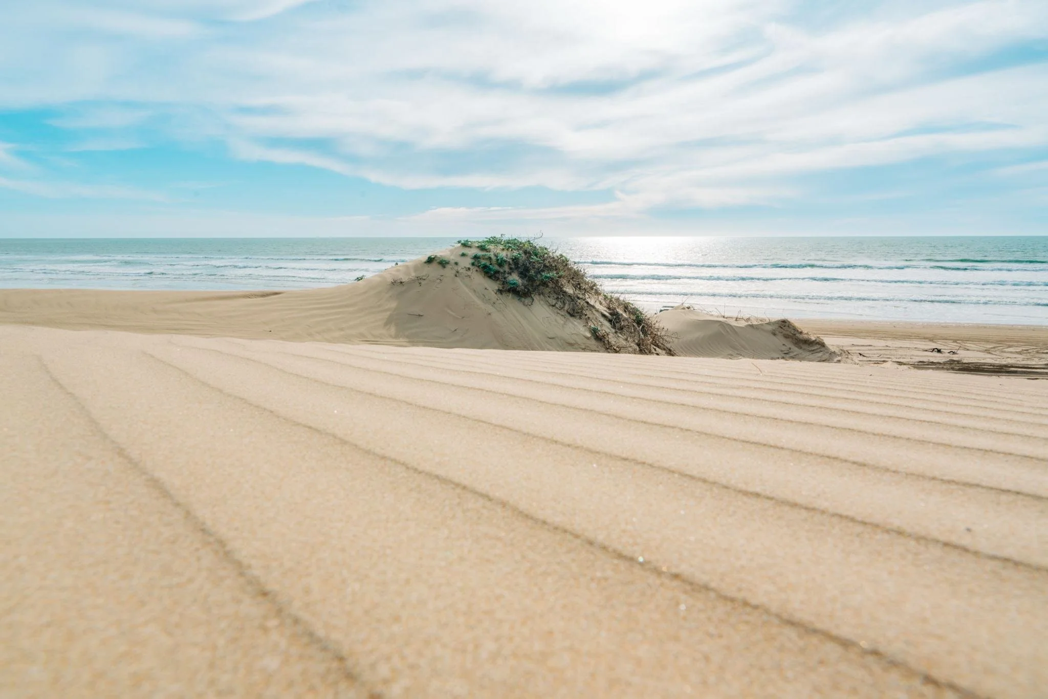 A sandy beach with sand dunes and the ocean in the background under a partly cloudy sky.