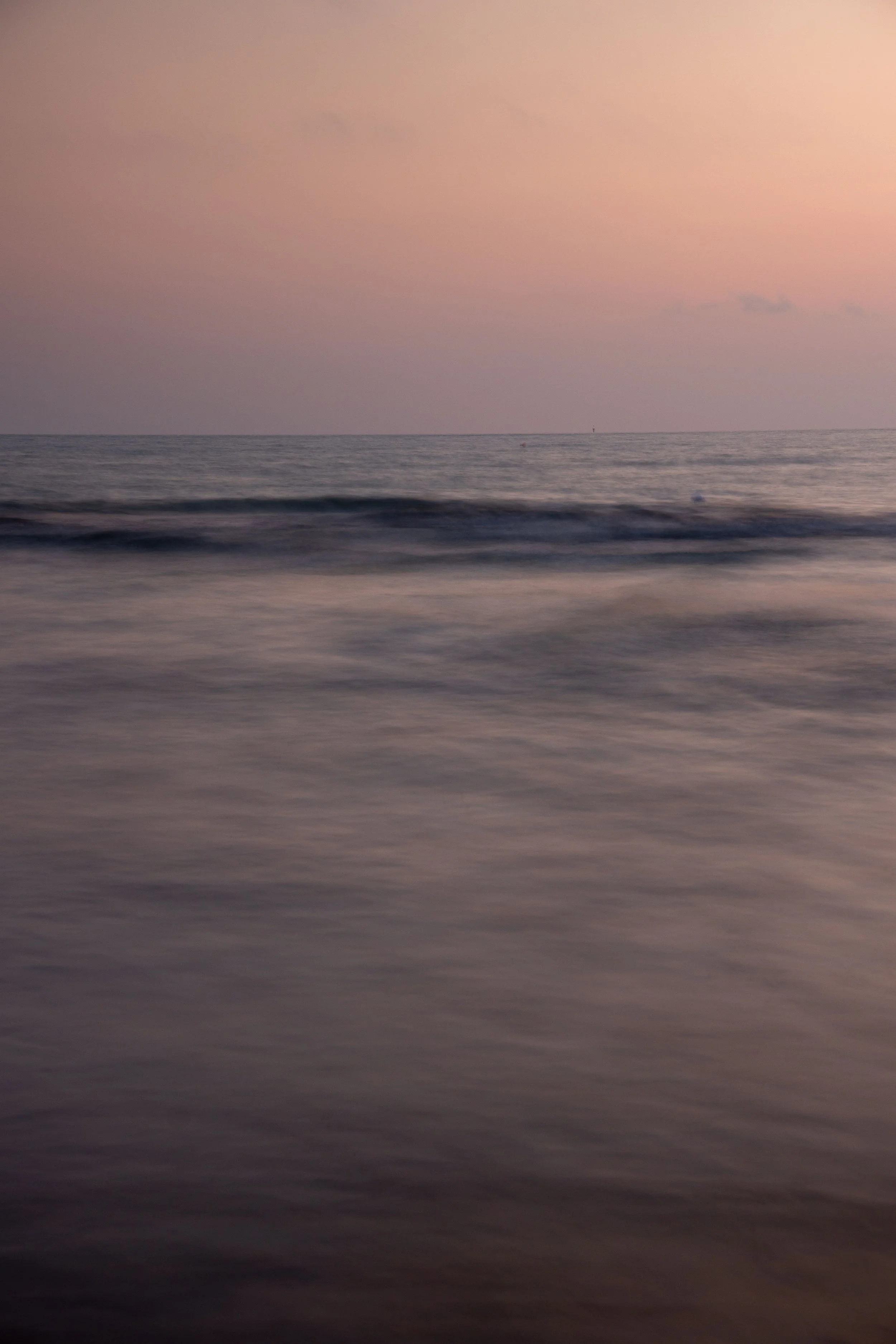 Ocean waves beneath a soft pink sunset sky