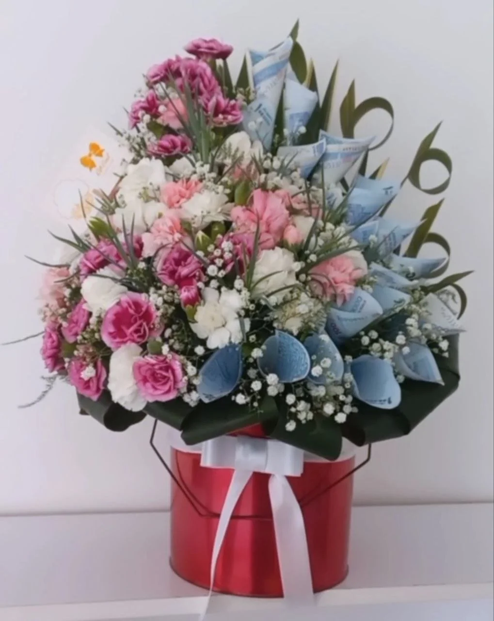 Flower bouquet with pink, white, and purple flowers in a red container, decorated with a white ribbon.