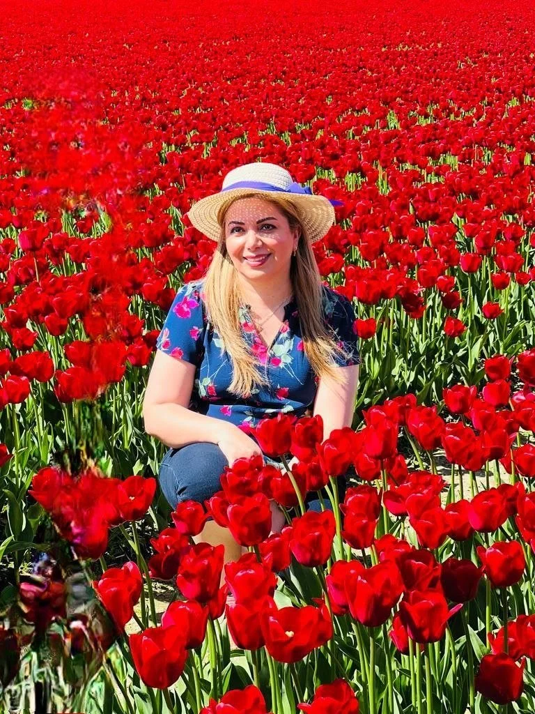 The bloom basket florist wearing a straw hat and a floral shirt is sitting in a large red tulip field on a sunny day.