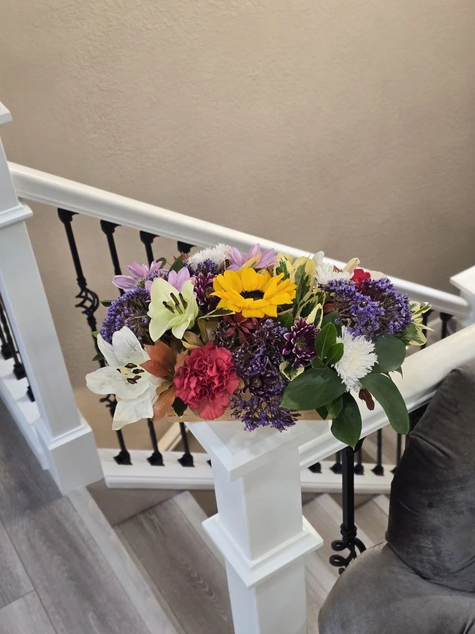 A bouquet of various colorful flowers resting on a white stair newel post inside a house.
