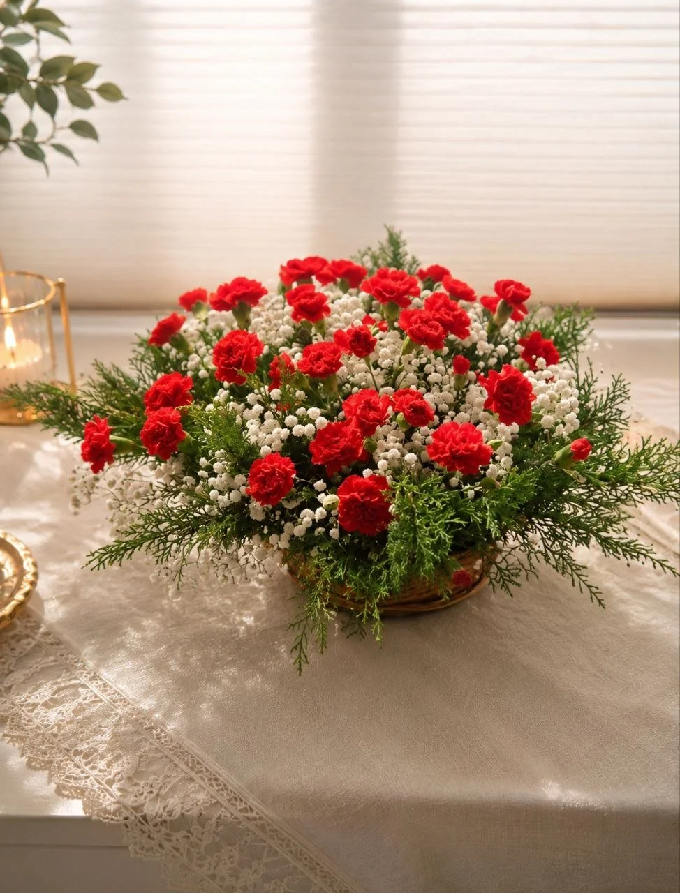 A Luxury sympathy arrangement  of red carnations and white baby's breath in a basket on a lace-trimmed table cloth.