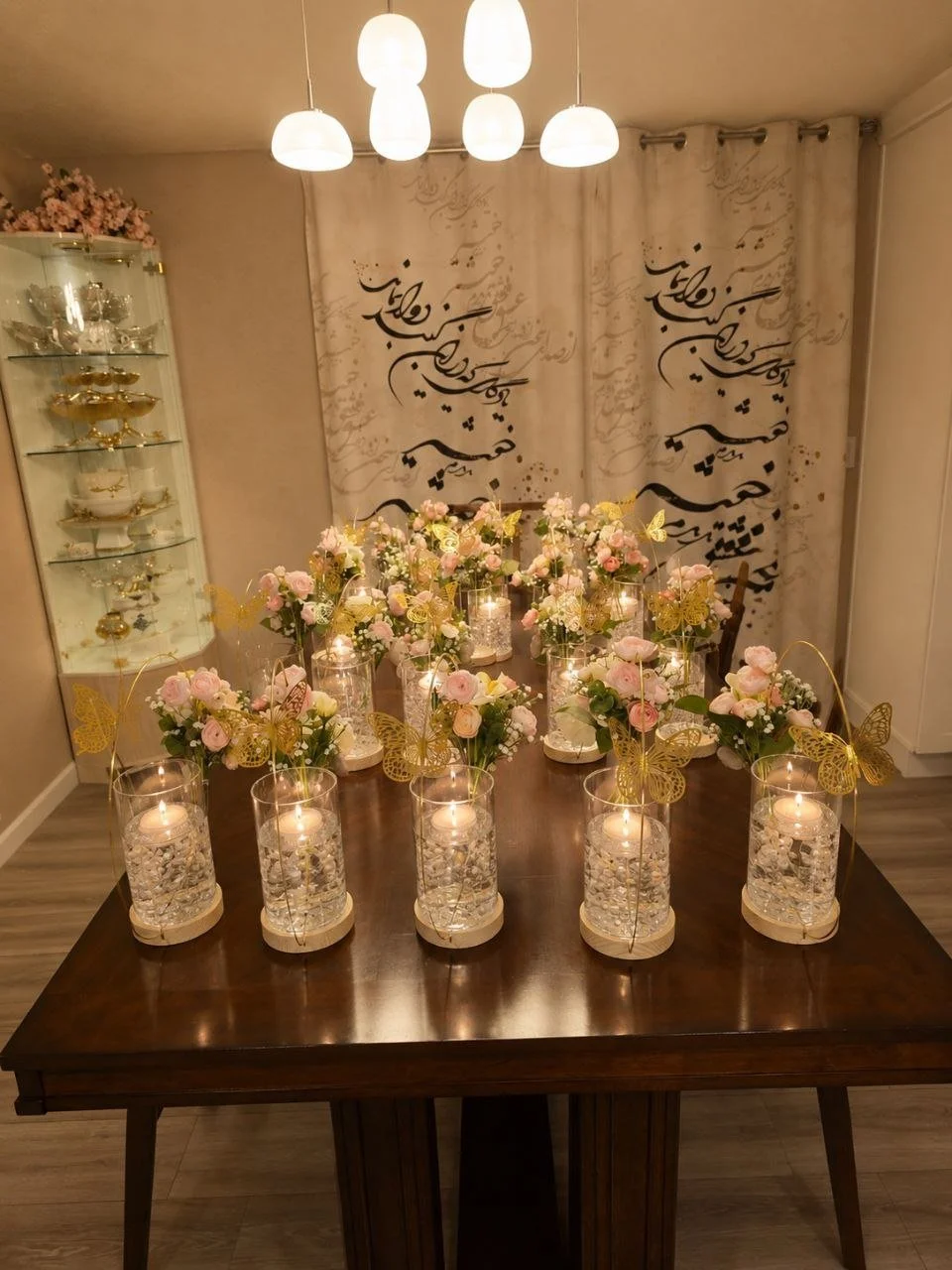 Table decorated with pink and white flowers, floating candles, and gold butterfly ornaments in a dining room.