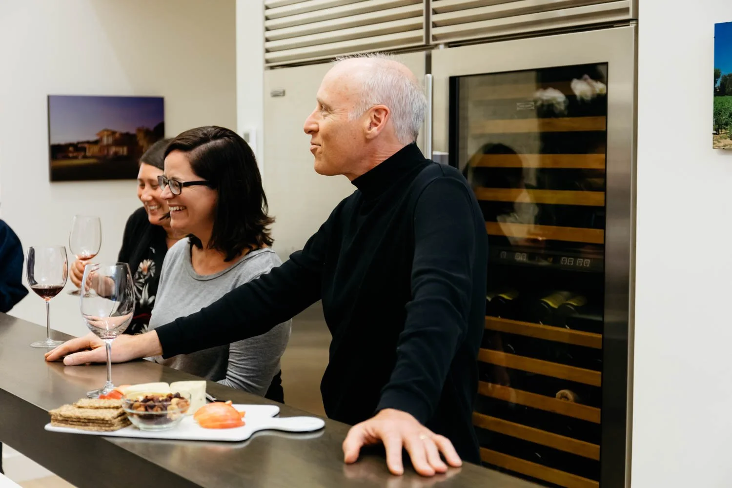 People enjoying a social gathering in a modern kitchen with wine glasses and cheese platter on the counter.