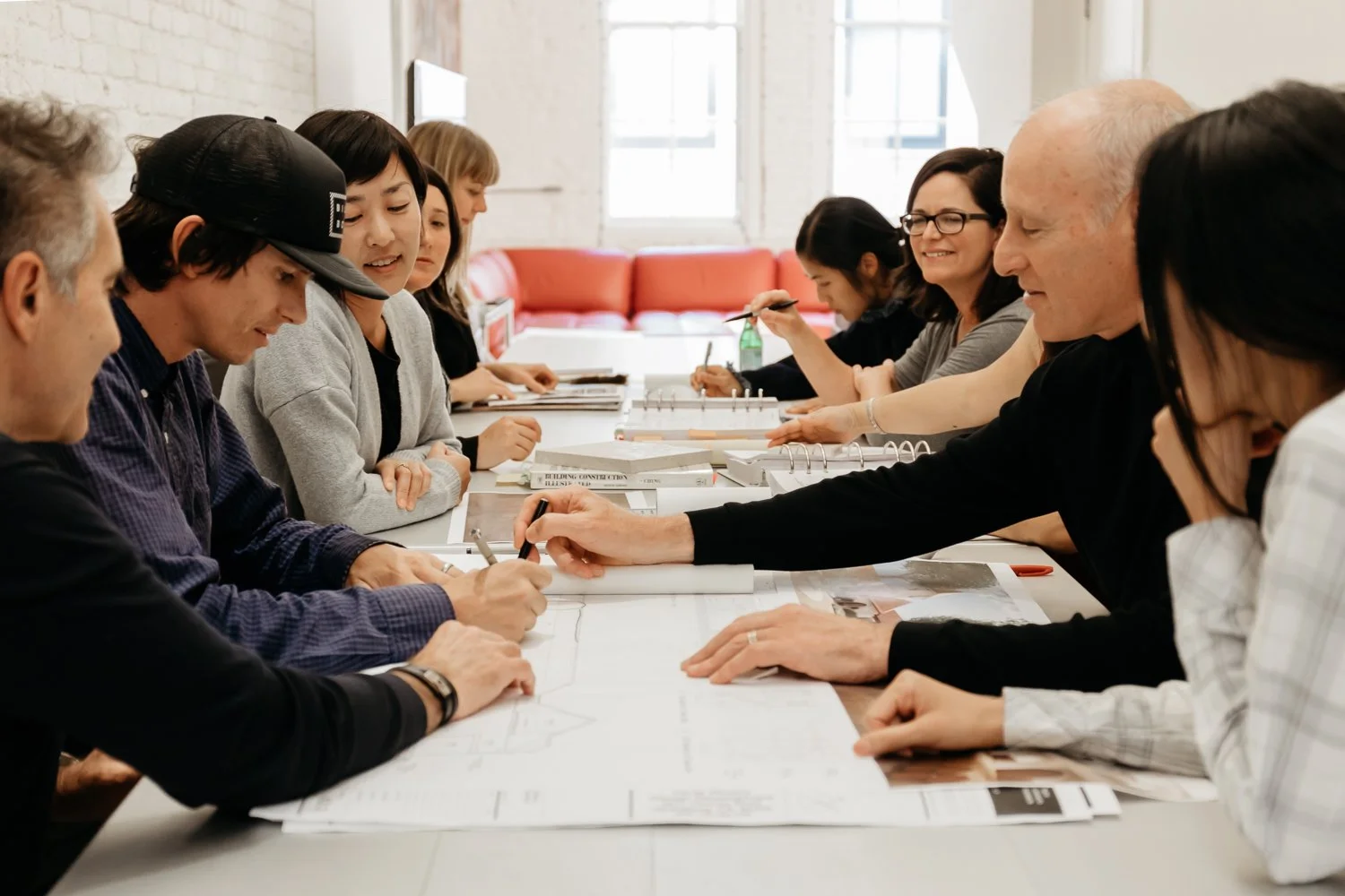 Group of diverse people around a table working on architectural plans and sketches in a well-lit room.