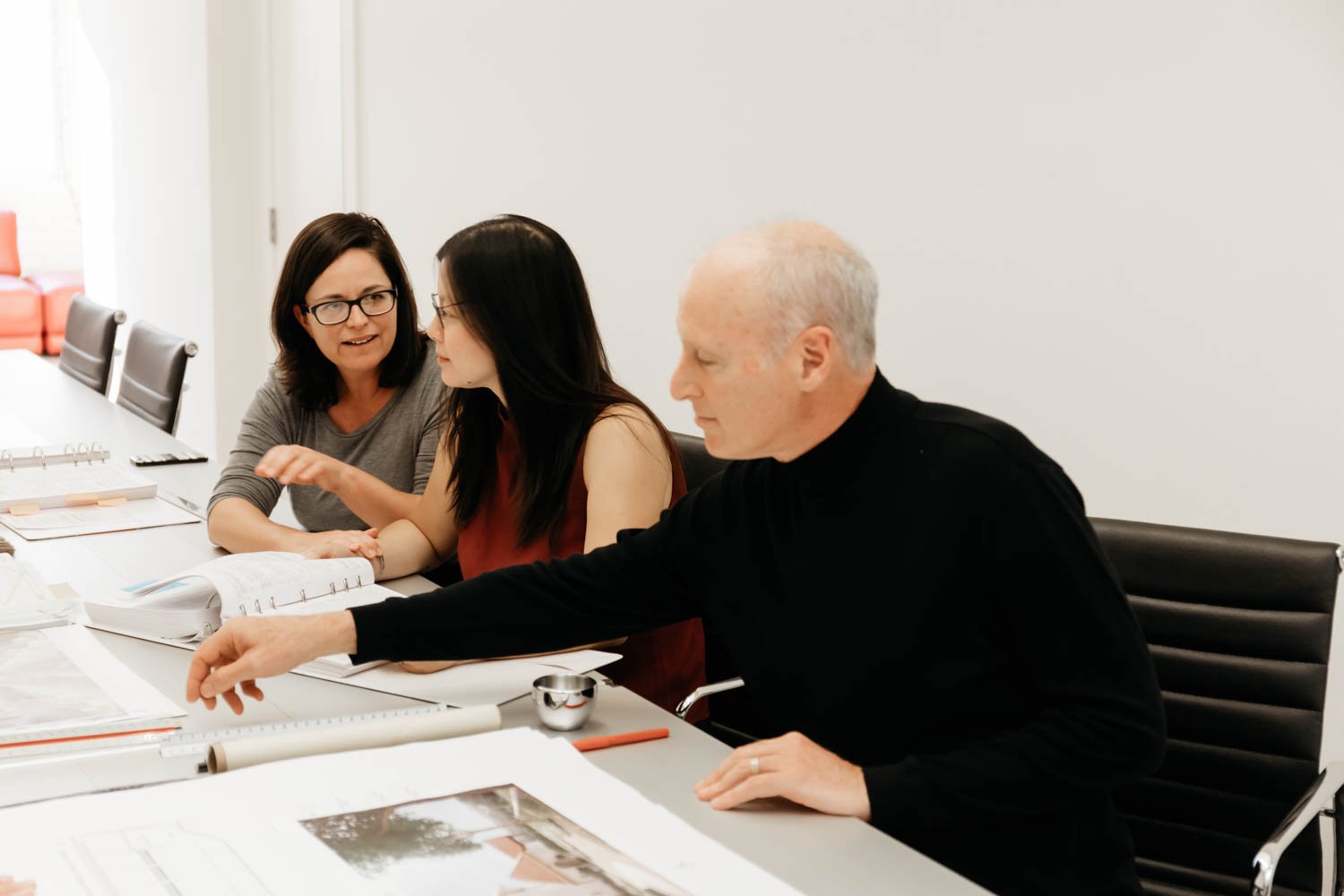 Three people, two women and a man, sitting at a conference table discussing documents and plans.